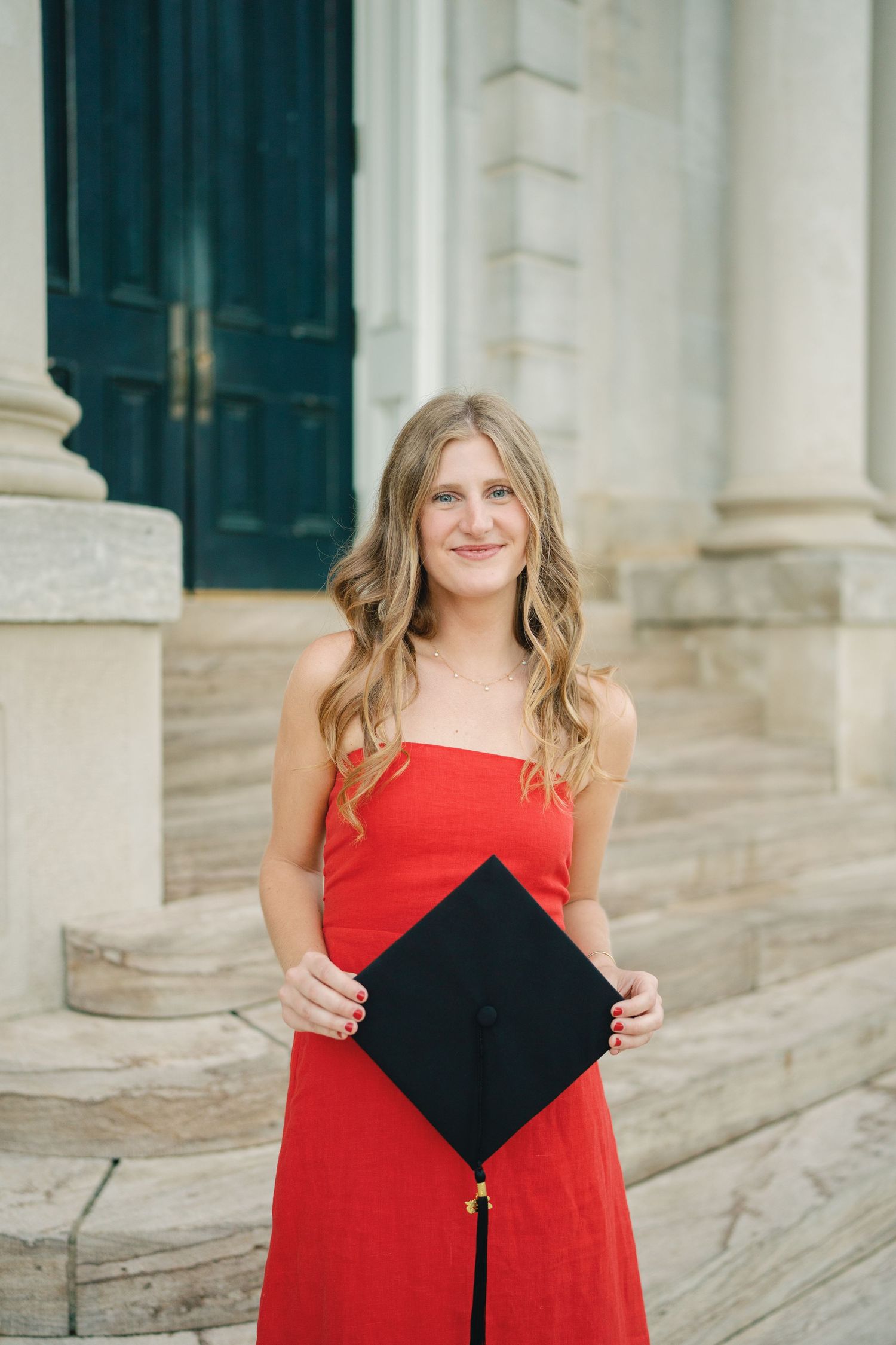 Graduate in red dress poses with graduation cap against stone columns in series of celebratory photos.
