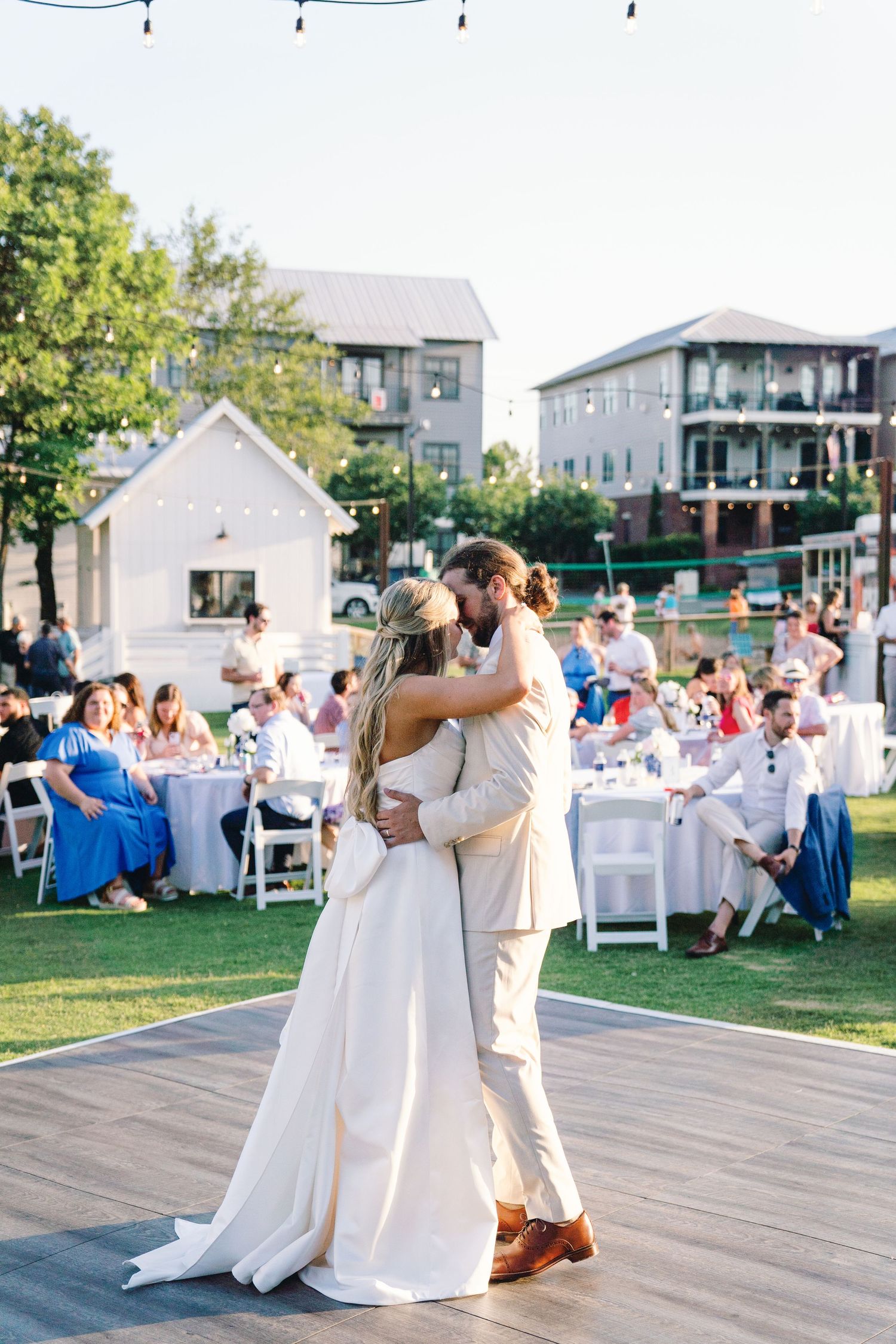 Couple dancing at an outdoor wedding reception on a wooden deck with white tables in background.