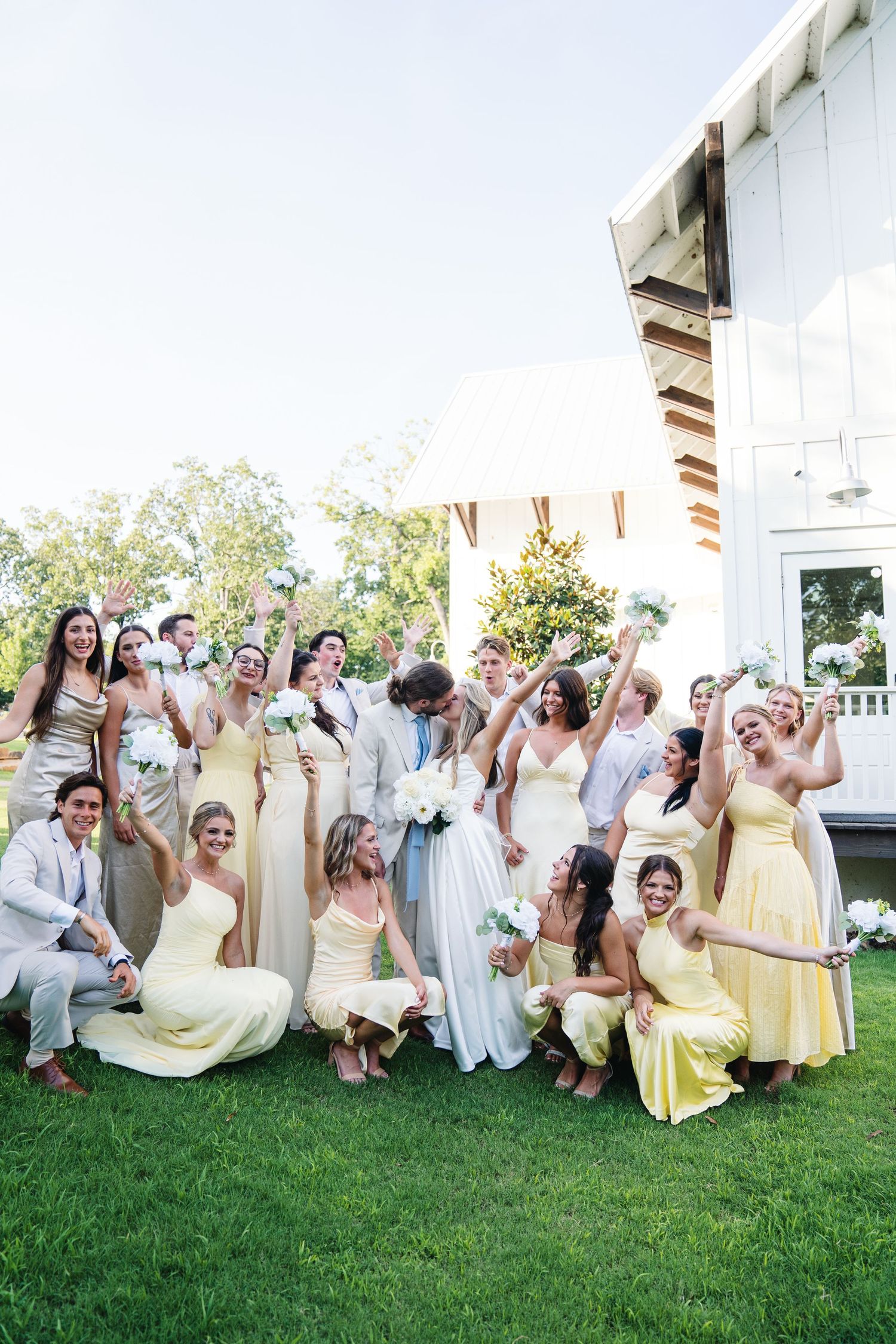 Wedding party celebrates on lawn with mix of white and yellow attire.