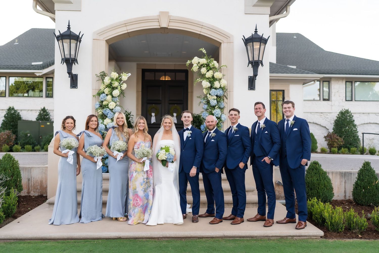 Wedding party poses for formal photos outside a white building with columns.