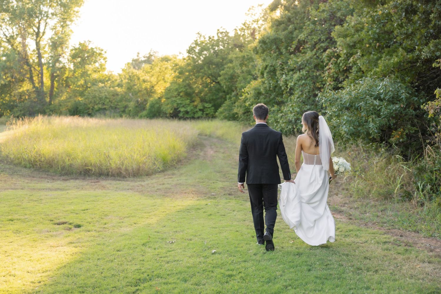 Wedding couple walking through a sunlit meadow during golden hour photography session.