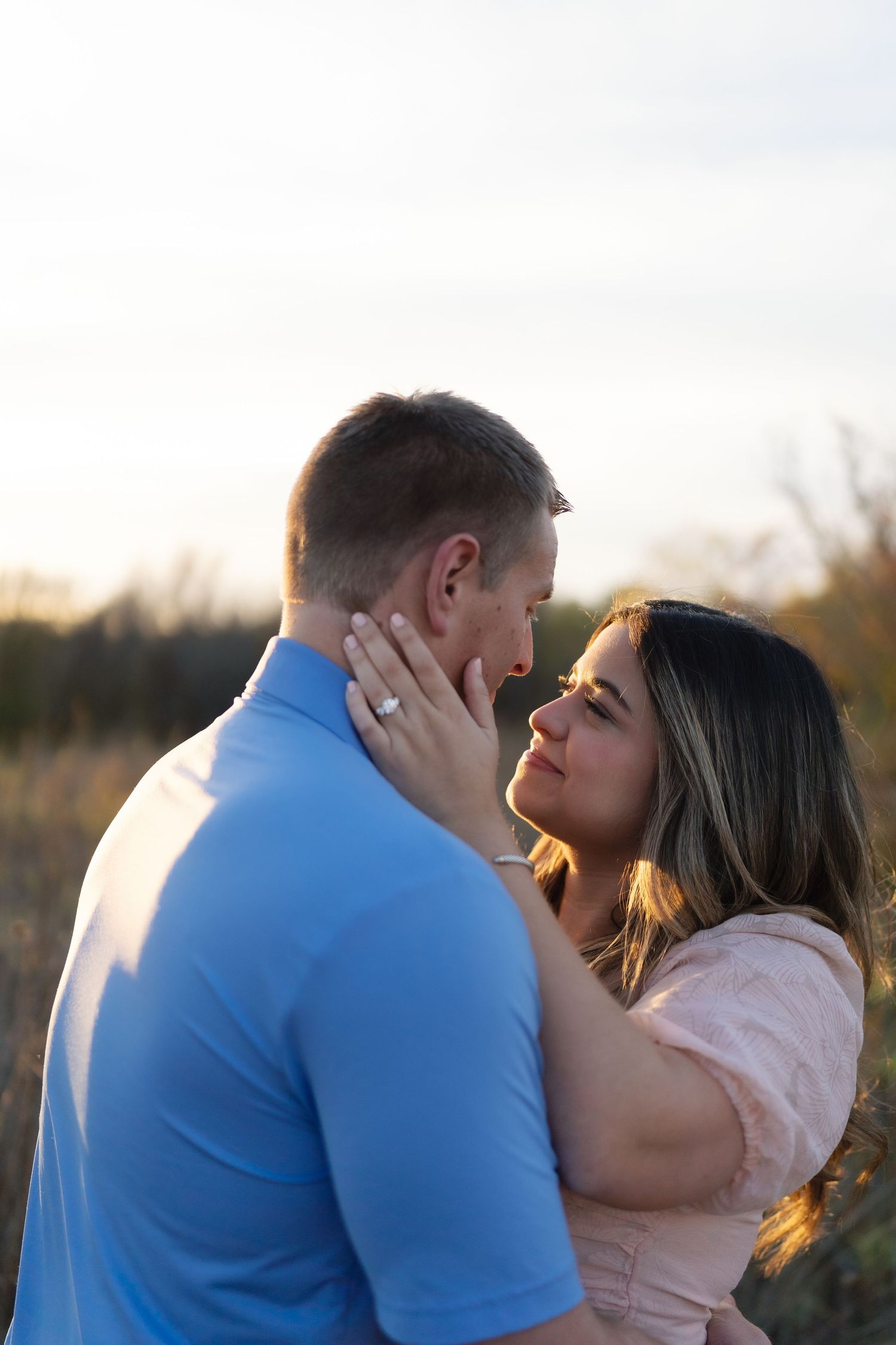 A couple shares an intimate embrace during sunset in a natural setting.