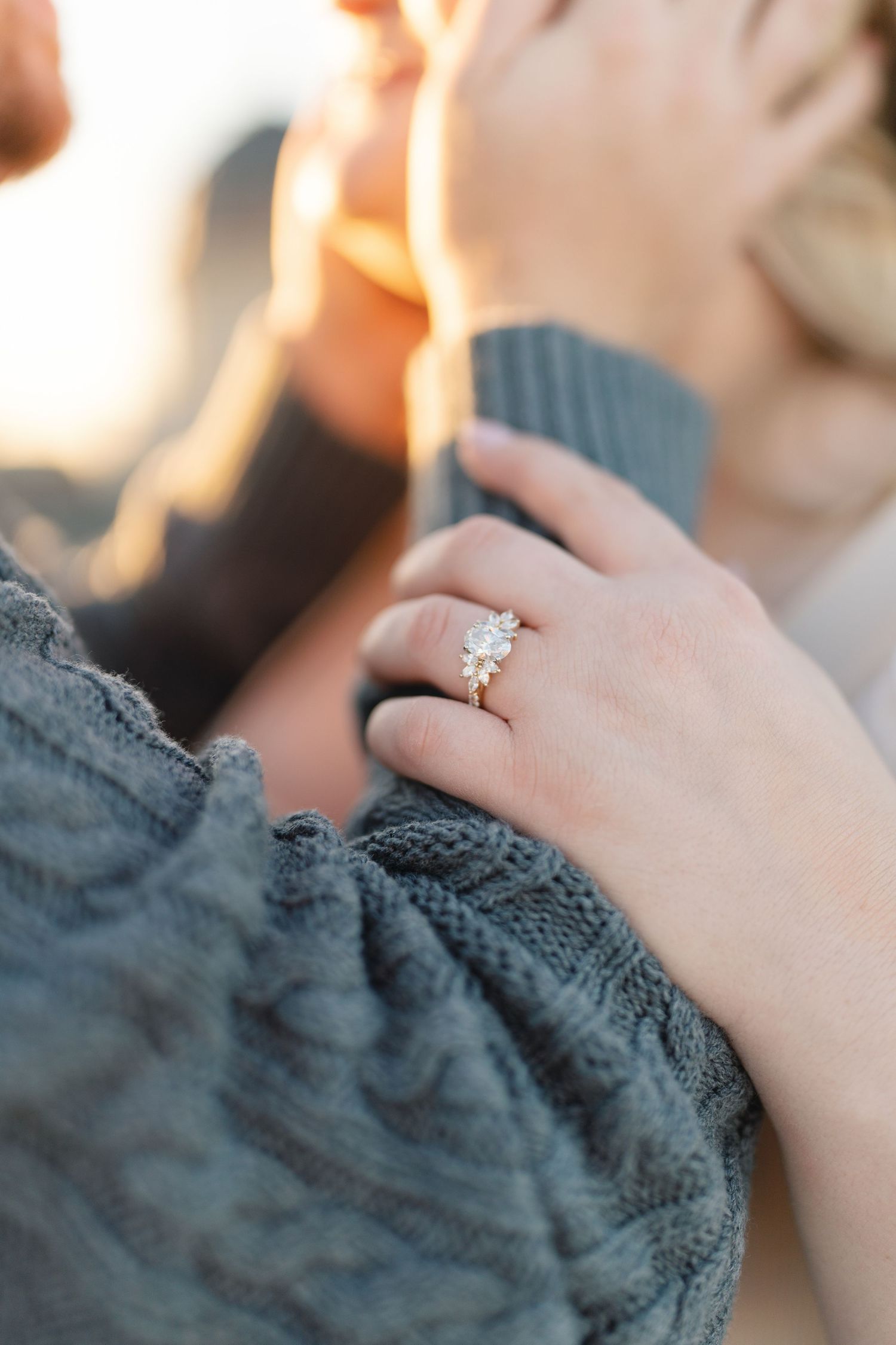 Close-up of engagement ring on hand against gray knit fabric.