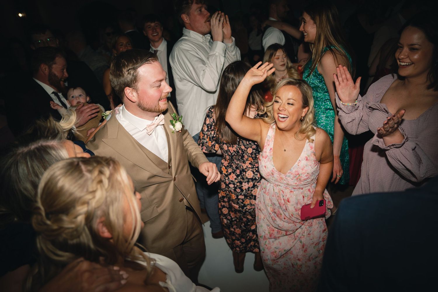 Wedding guests dancing and celebrating on a dimly lit dance floor.