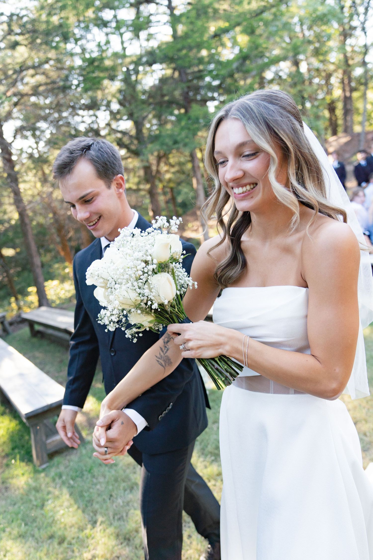 Wedding party members laughing and smiling while holding delicate white bouquets outdoors.