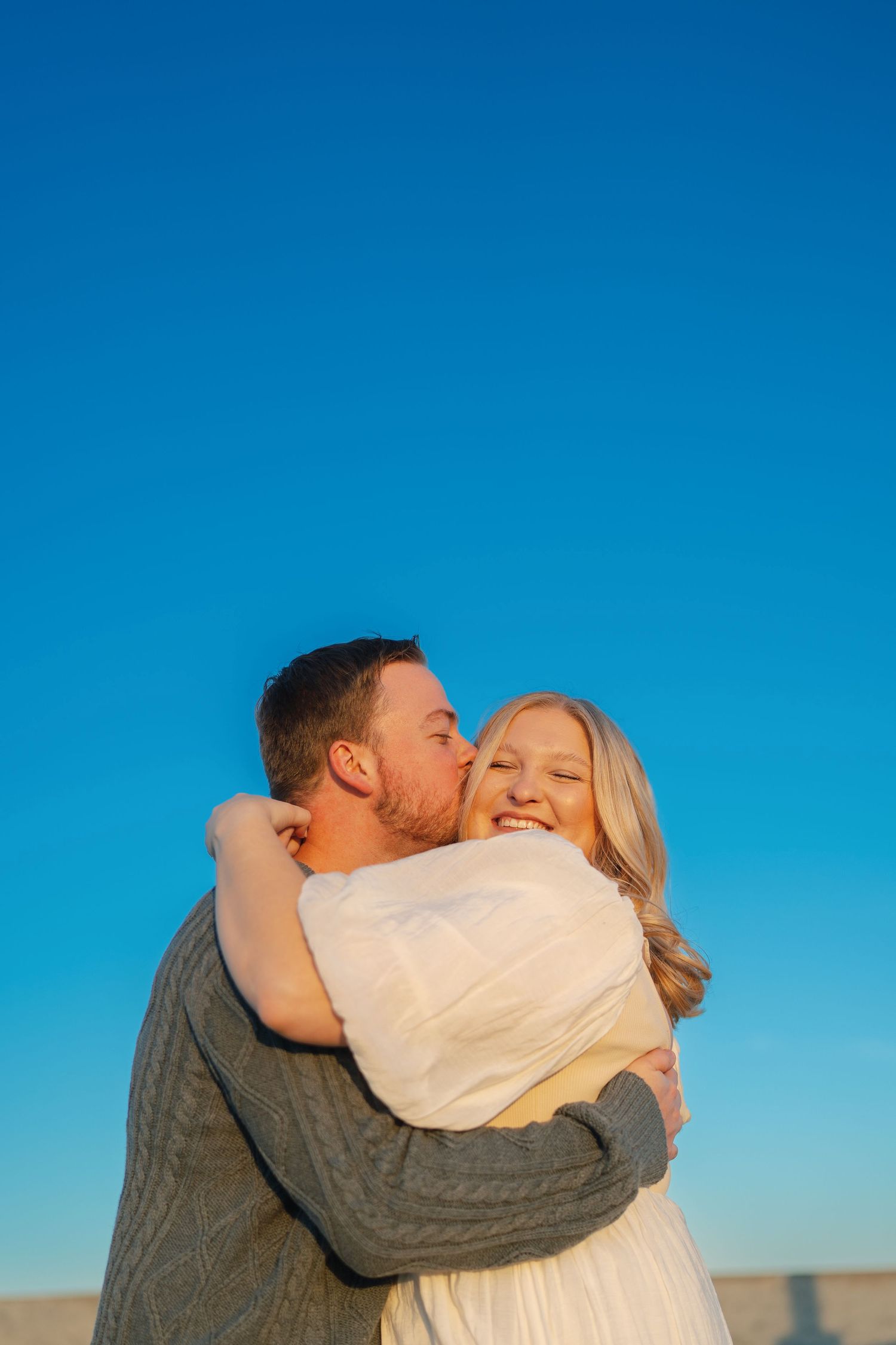 Intimate embrace against vibrant blue sky during golden hour.