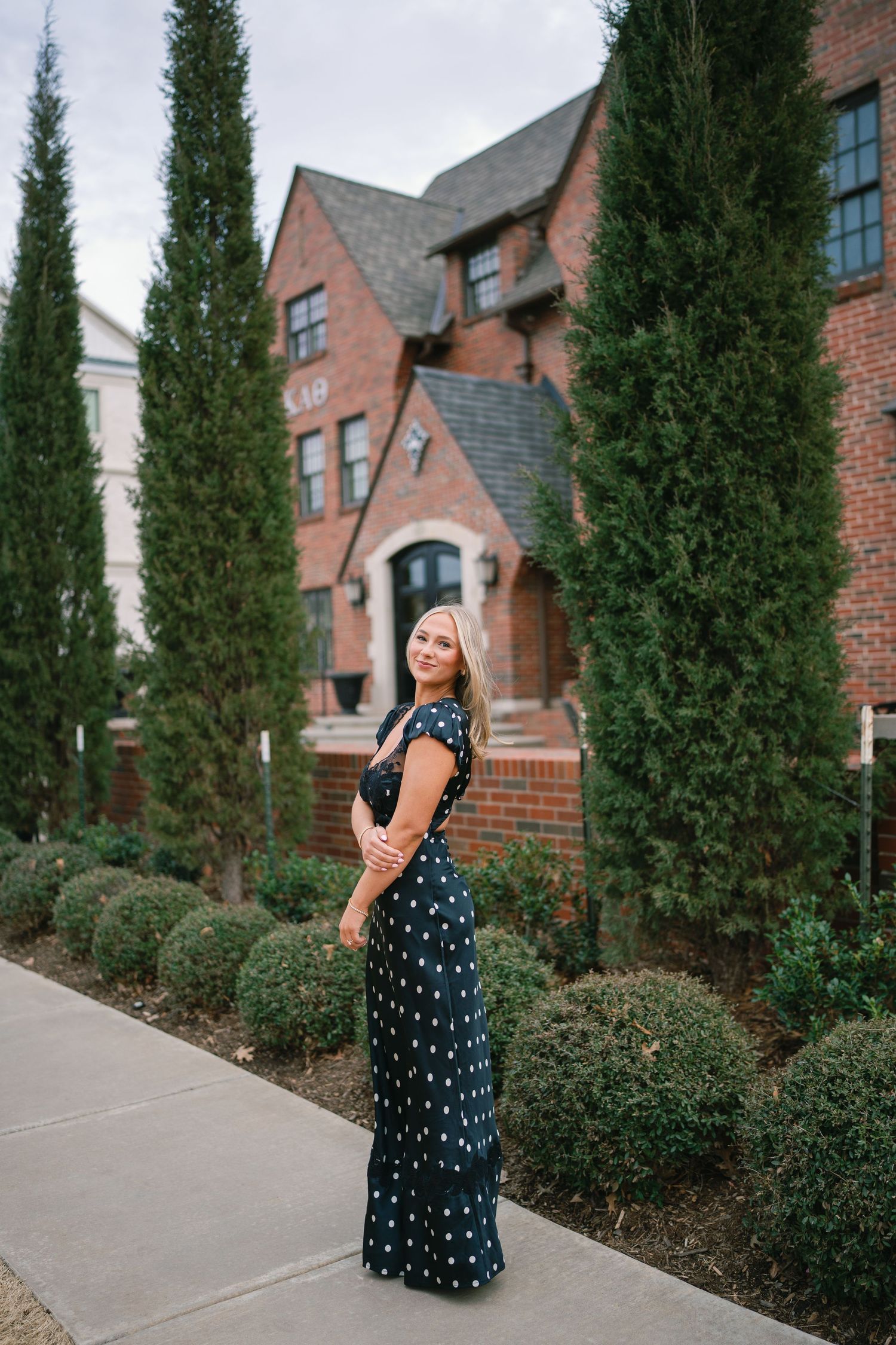 A polka dot dress photographed against brick buildings and cypress trees.