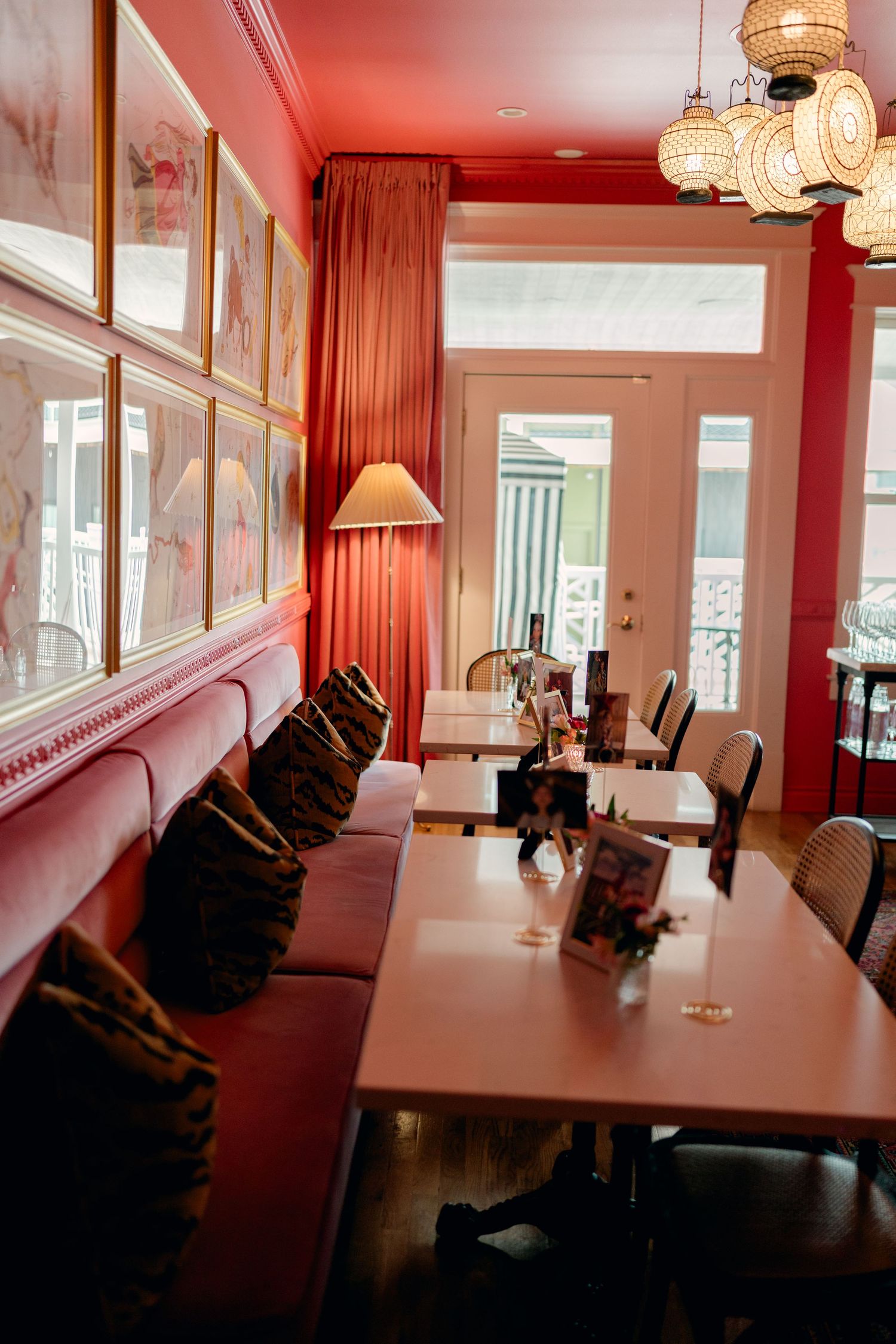Elegant restaurant dining room with pink banquette seating, red walls, framed artwork, and warm ambient lighting.