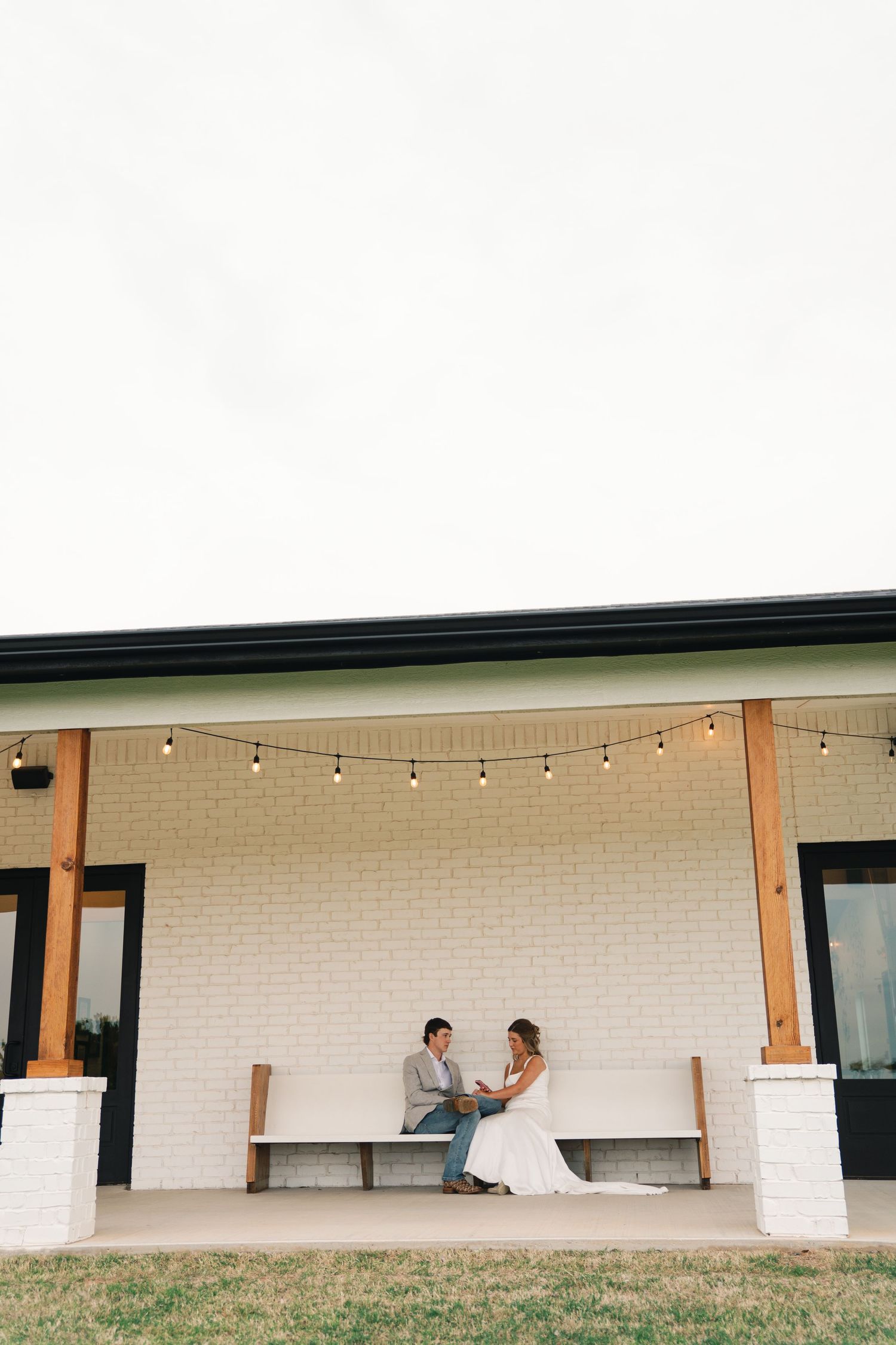A modern white building with wooden posts and string lights creating a minimalist outdoor space.
