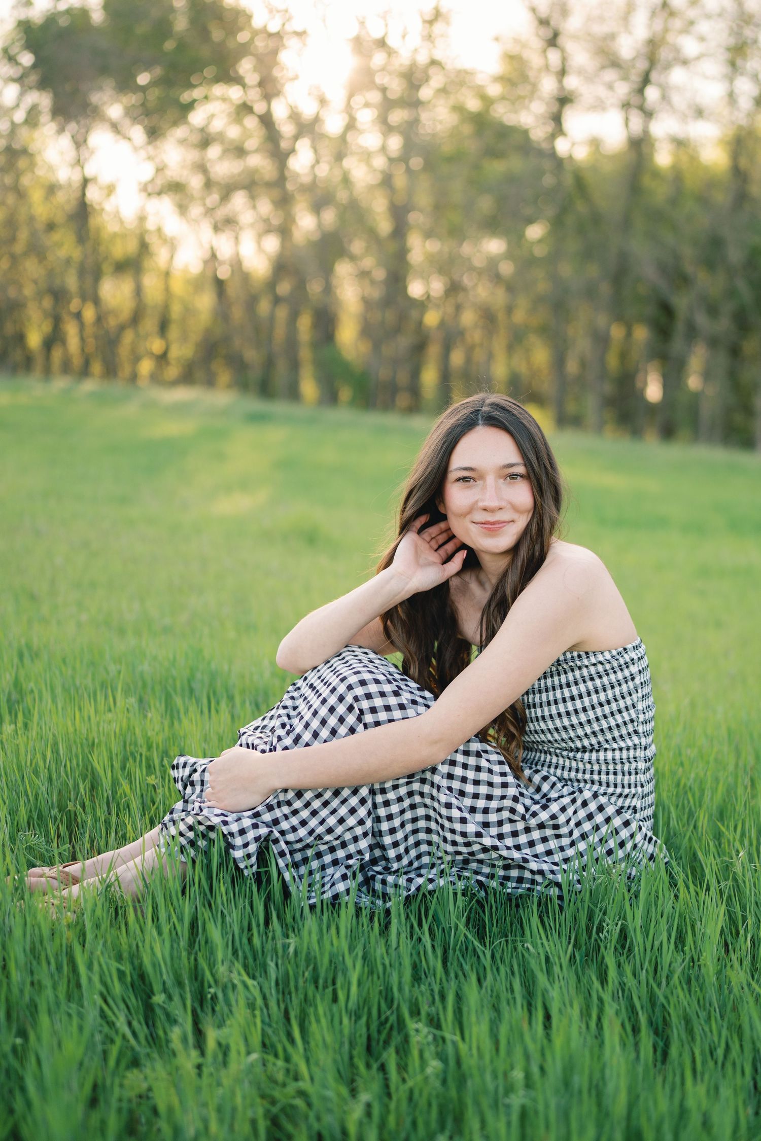 Person in gingham dress poses gracefully in tall green grass during sunset.