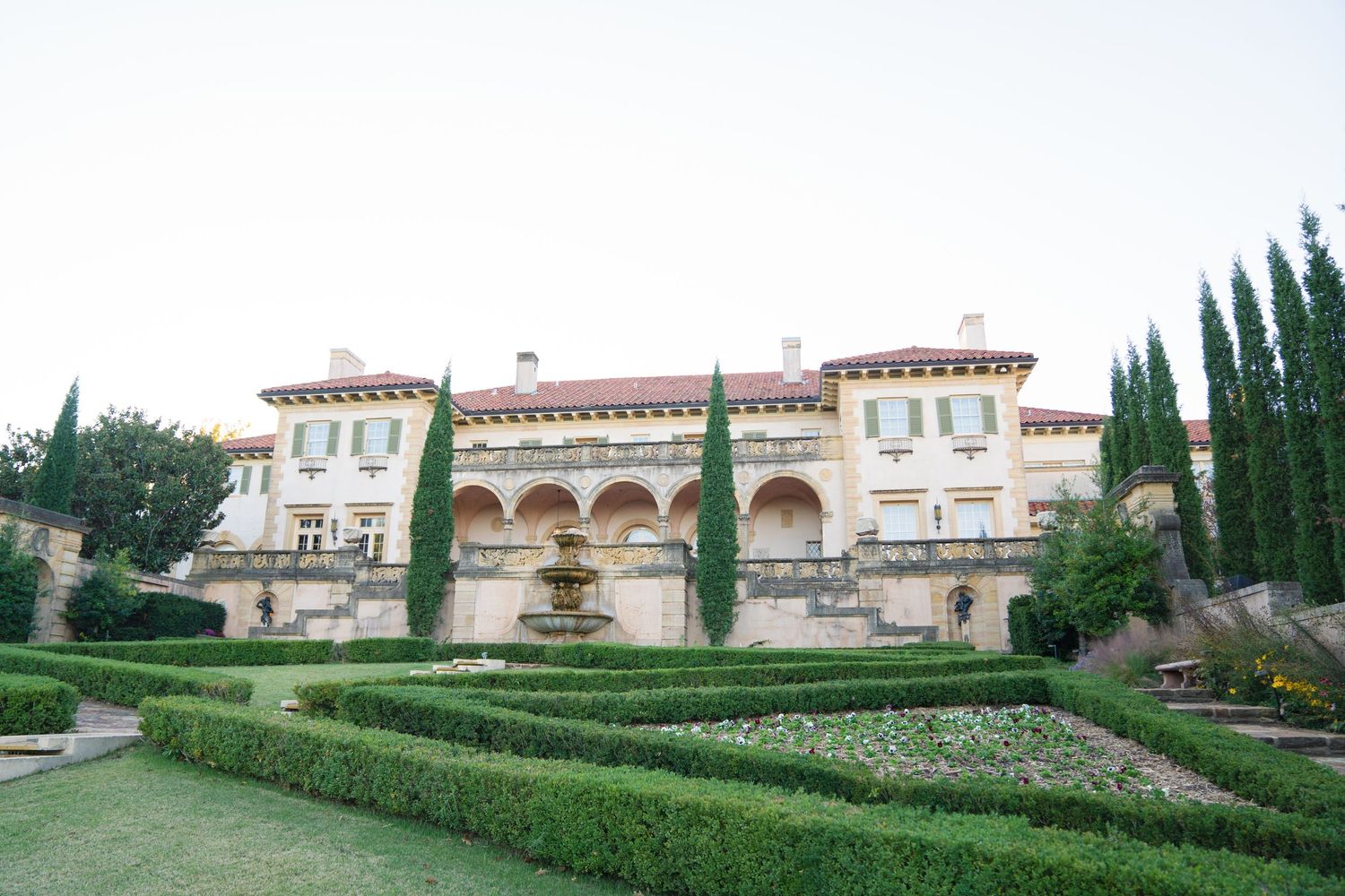 A panoramic view of an elegant Mediterranean-style villa with manicured gardens and cypress trees.
