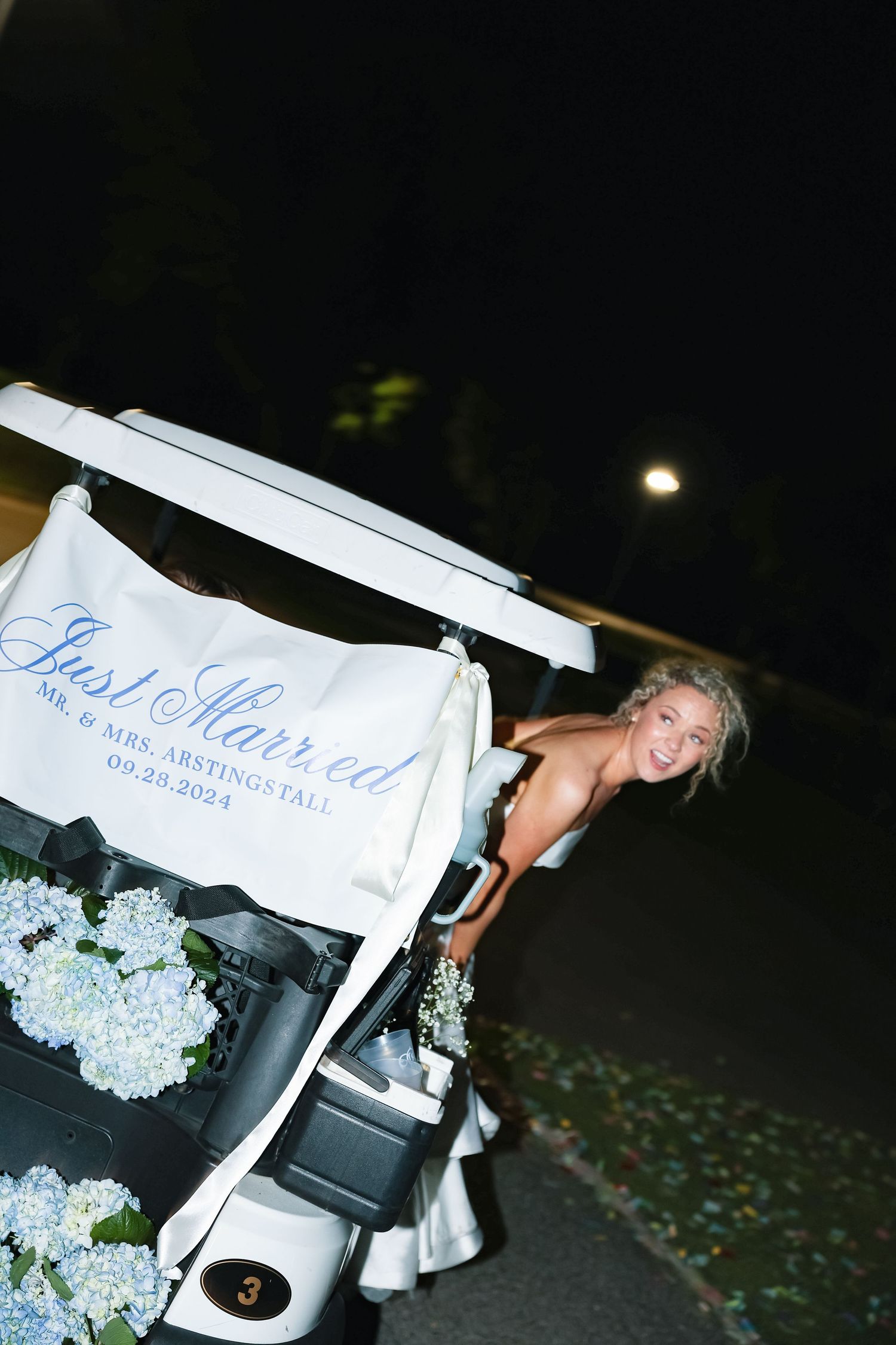 A decorated golf cart with hydrangeas and 'Just Married' signage at night.