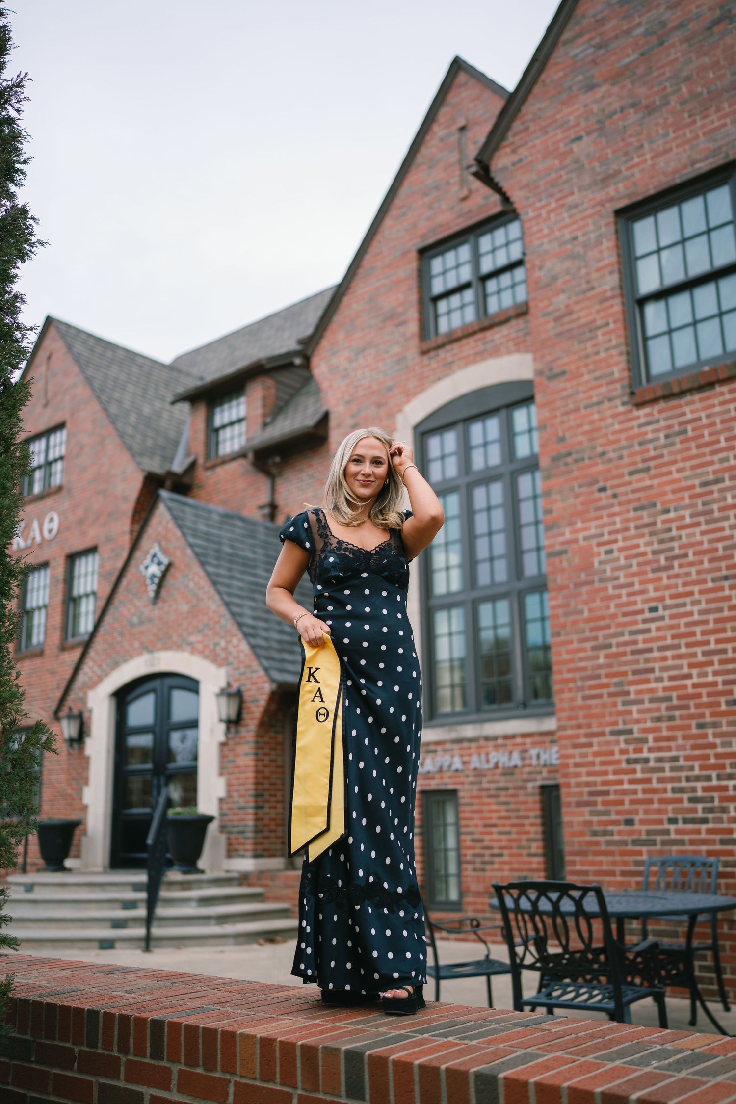 Person in polka dot dress posing outside brick building with architectural details.