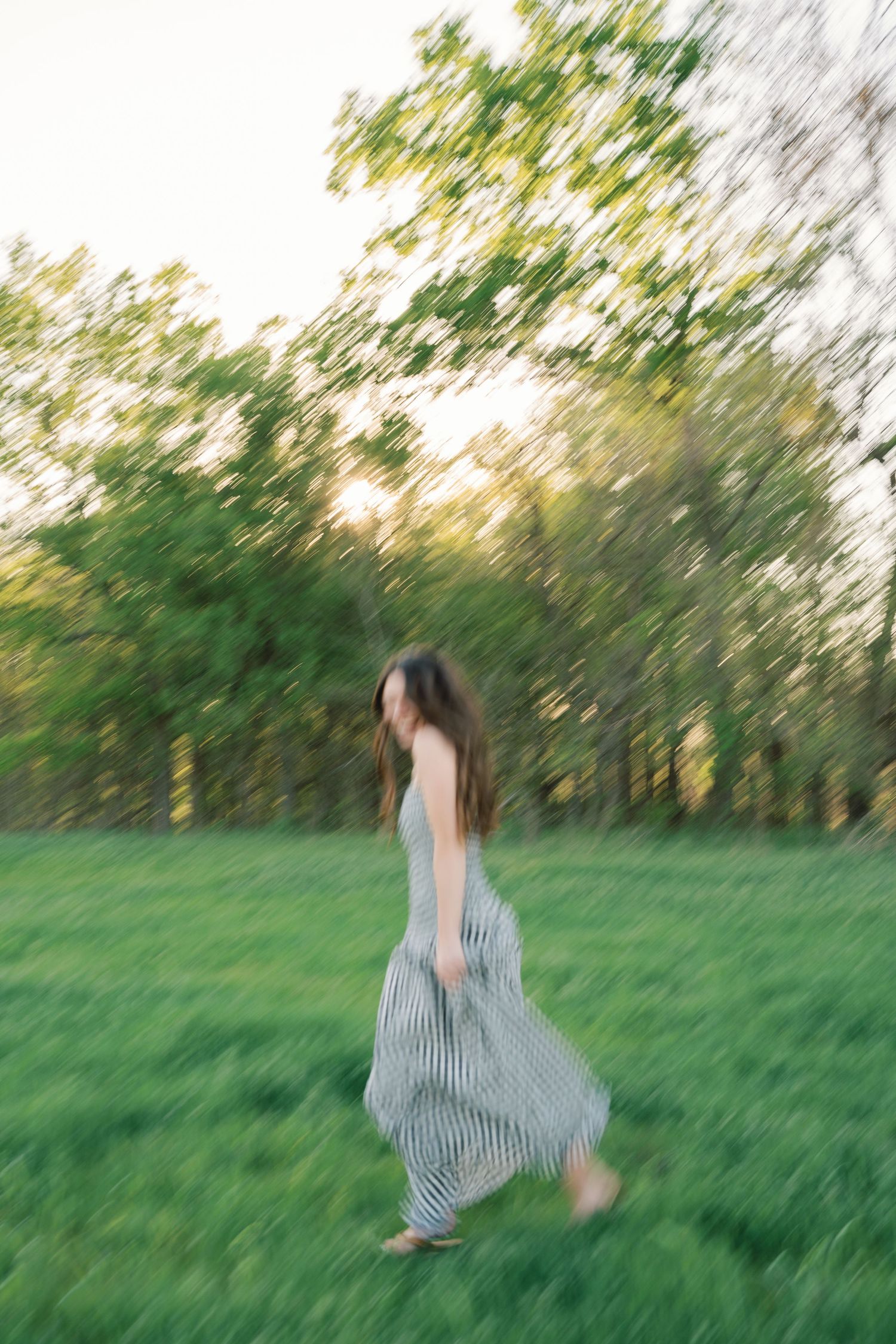 Figure in striped dress twirls joyfully in green field during golden hour.