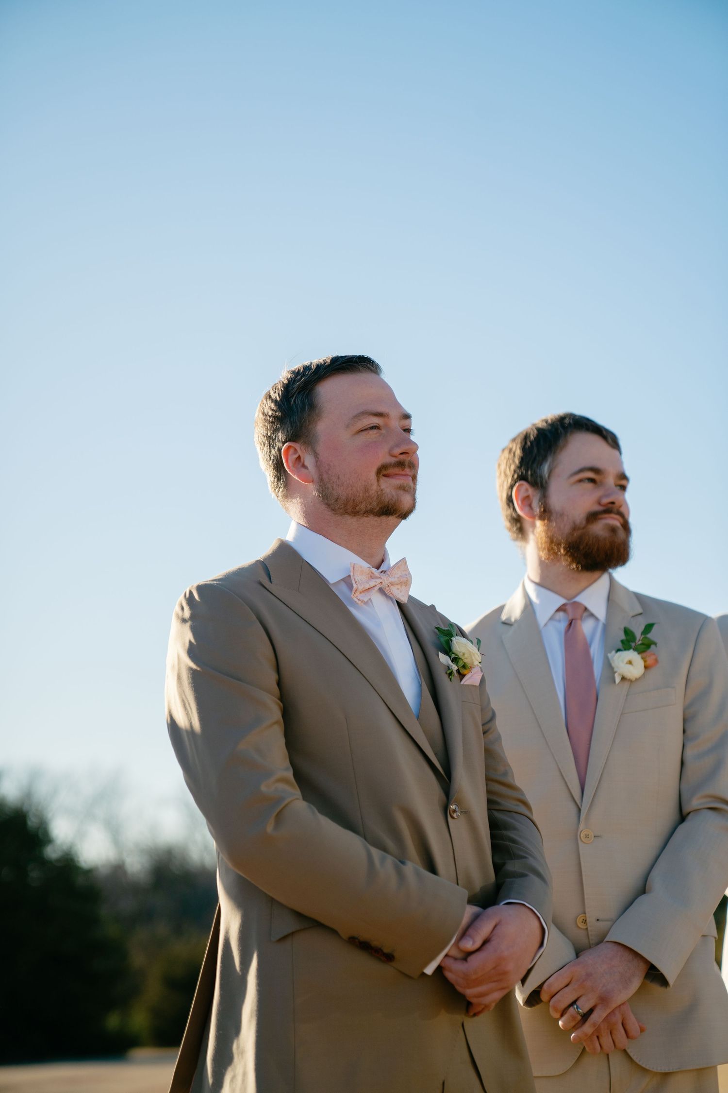 Groomsmen in tan suits pose together during golden hour outdoor wedding.
