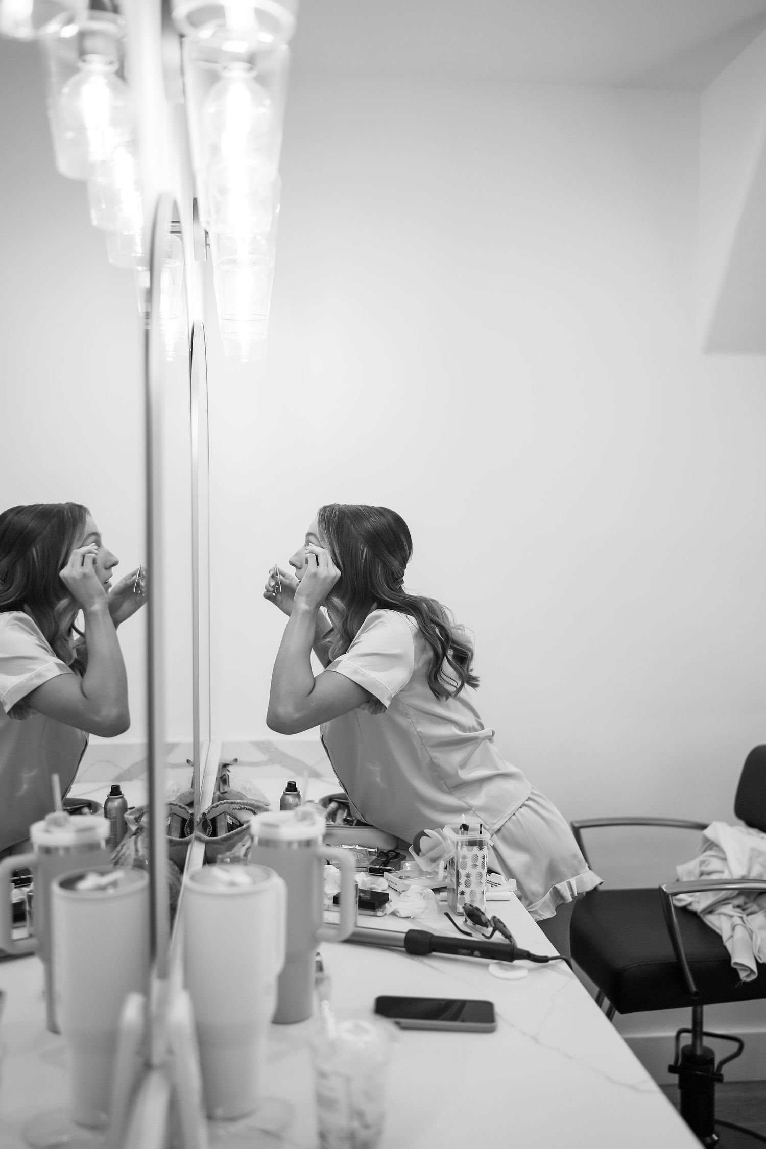 Black and white image of bridal preparation in a dressing room with bright vanity lights.
