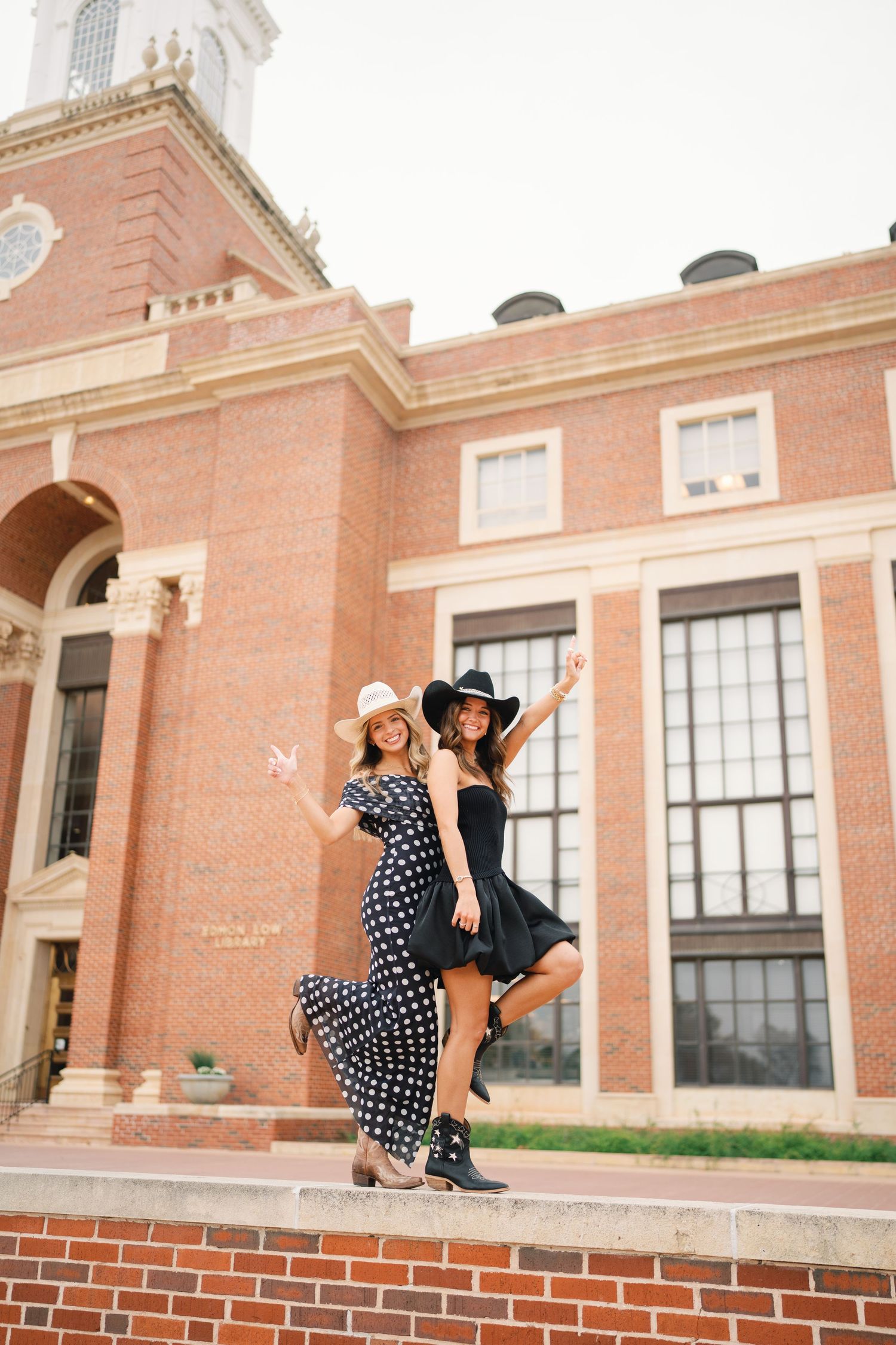 Two people in polka dot outfits share playful moment on brick wall of historic building.