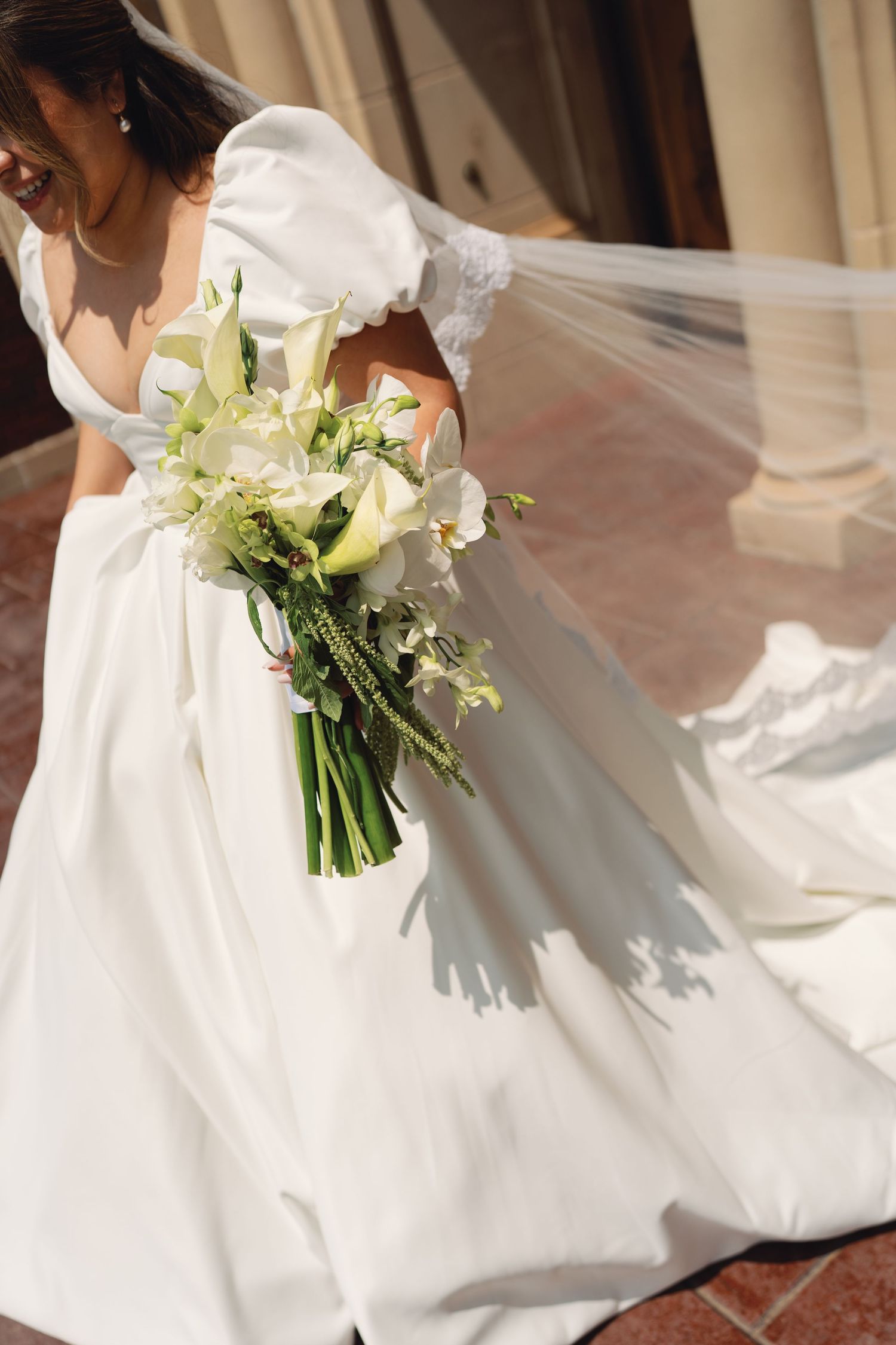 A bride in a flowing white wedding dress holds an elegant bouquet of white flowers and greenery.
