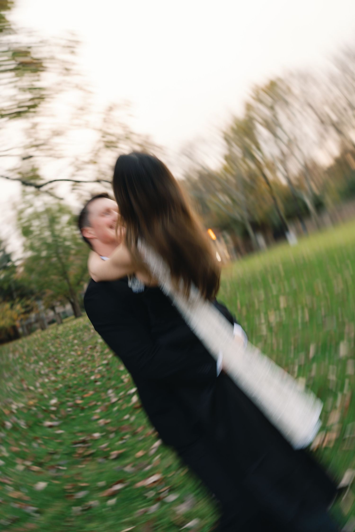 A blurred motion shot of two people spinning and embracing in a grassy outdoor setting during golden hour.