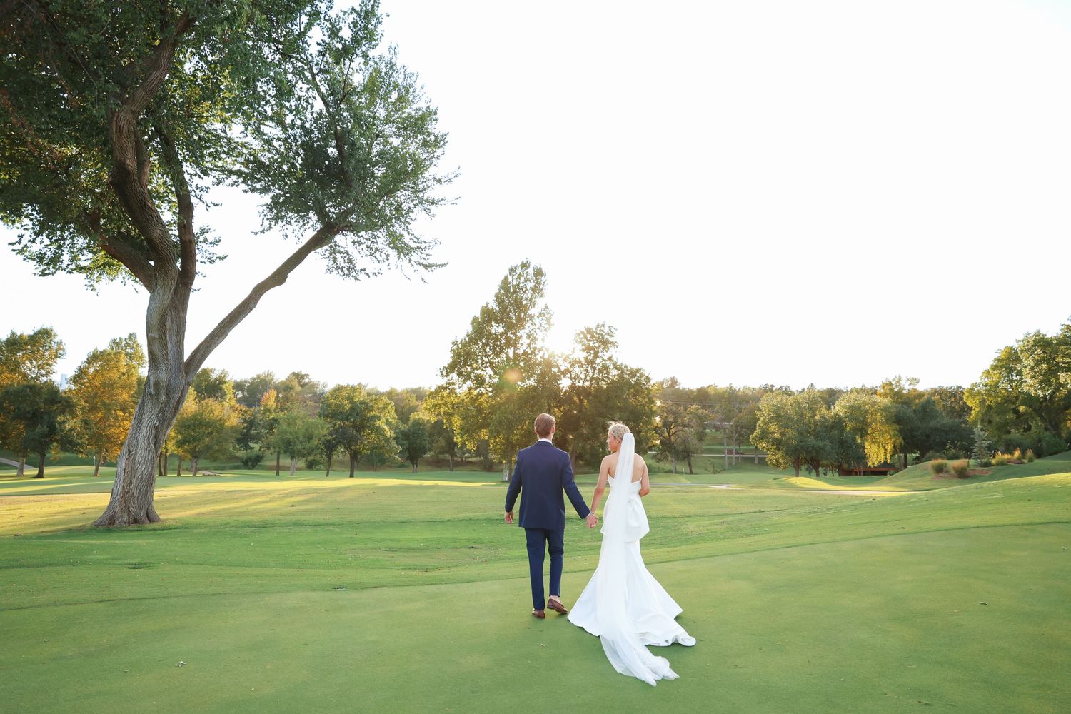 Newlyweds walk together across a scenic golf course at sunset.