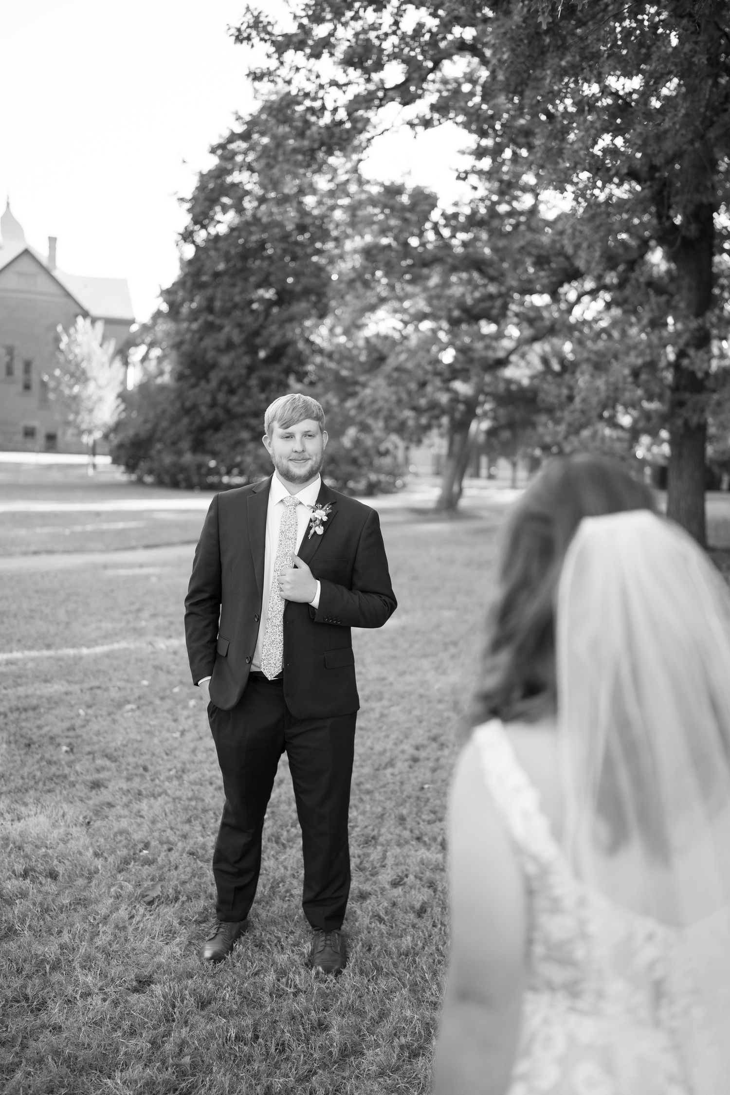 A wedding first look moment captured in black and white photography on a grassy lawn with trees in the background.