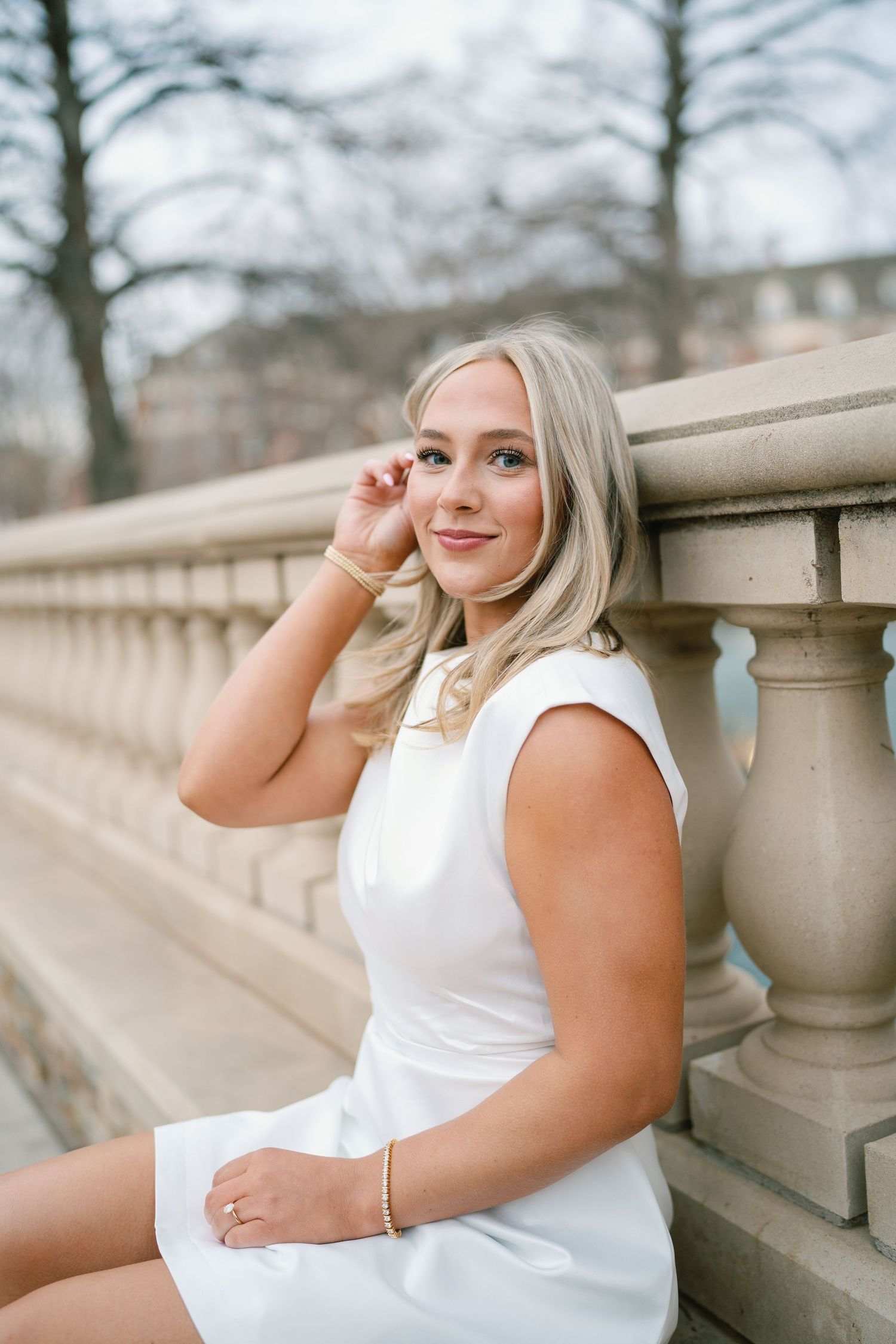 Person in white dress posing against stone balustrade during outdoor photo session.
