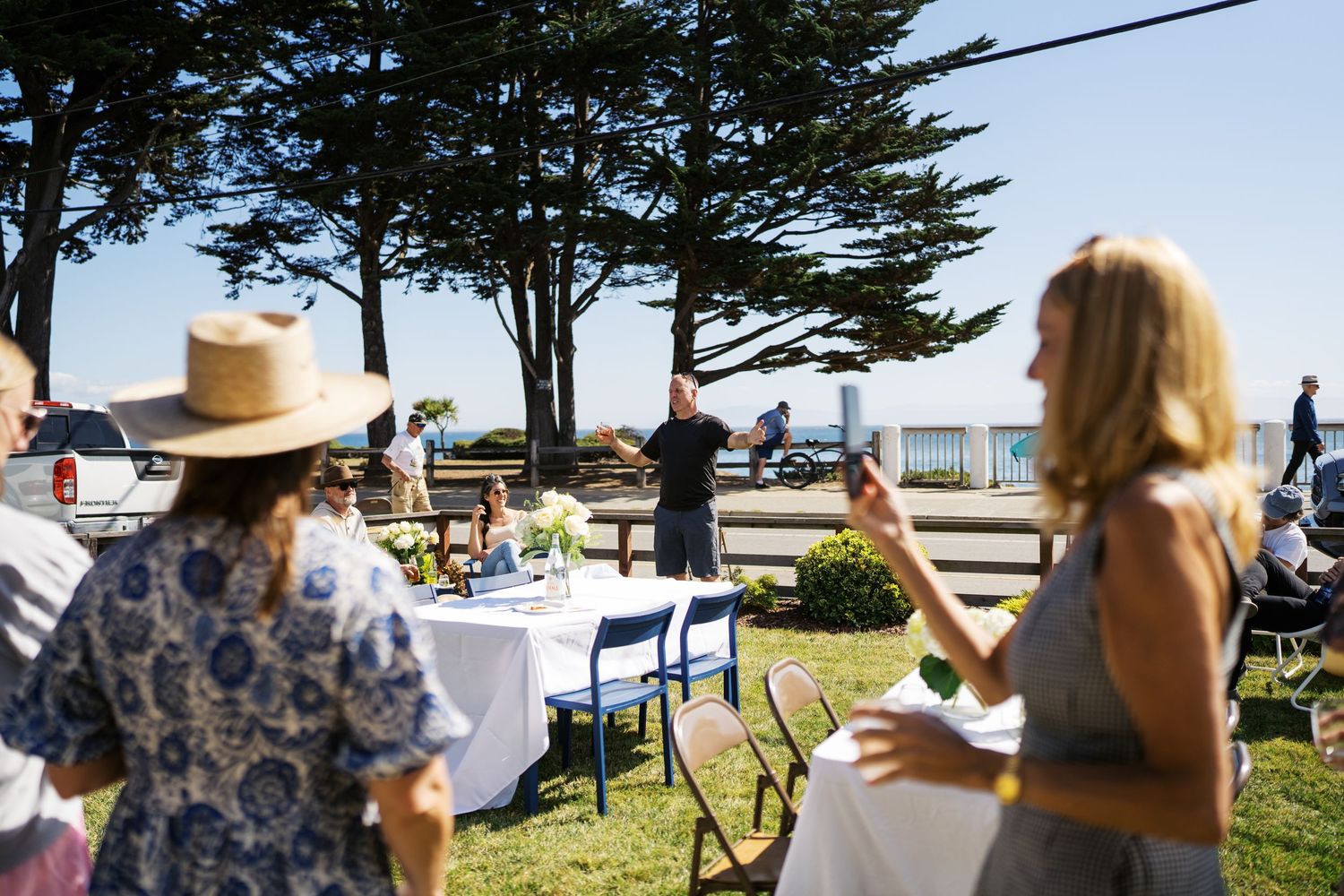 Guests seated at outdoor waterfront venue with pine trees and ocean view.