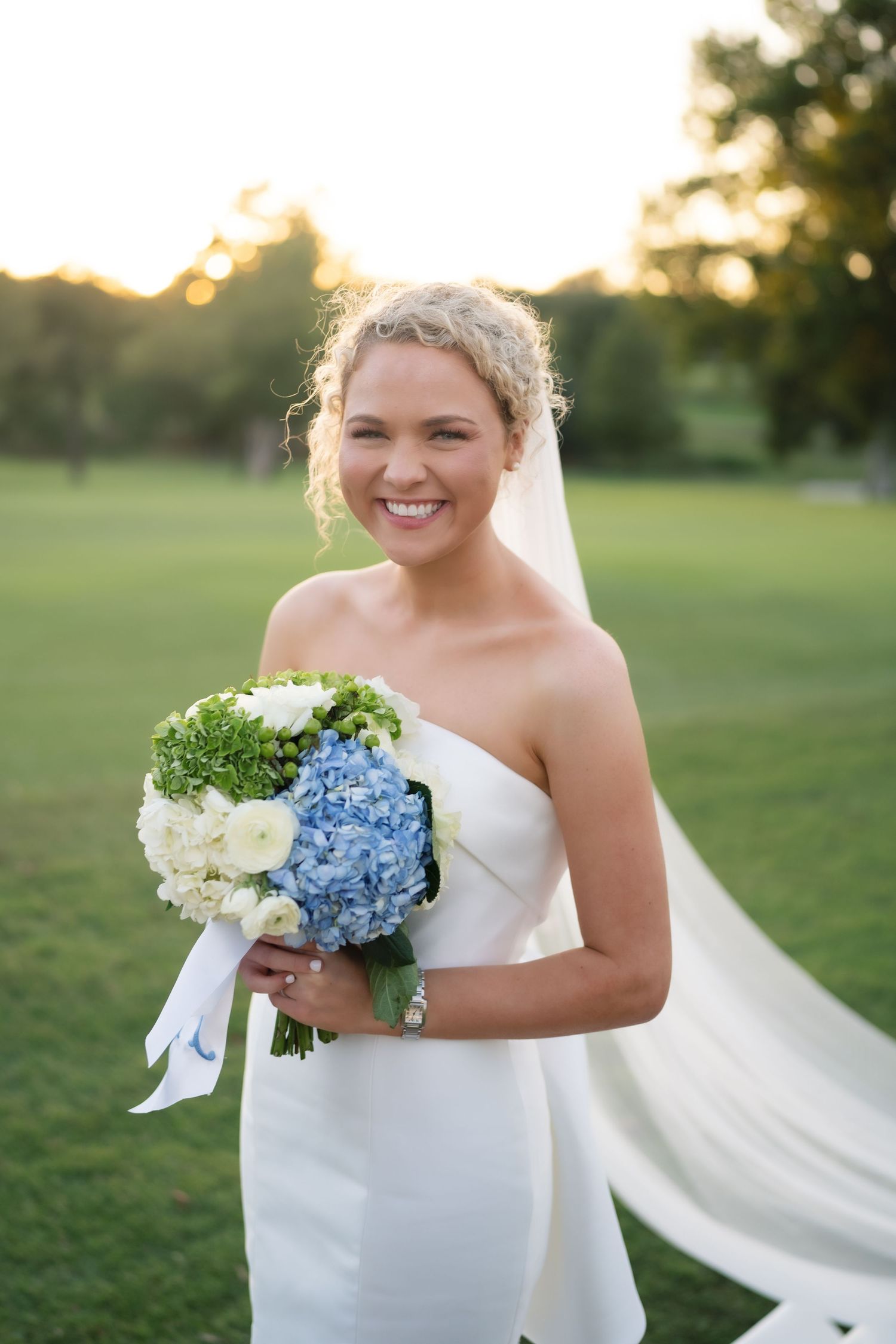 A bride holds a beautiful bouquet of white and blue hydrangeas with a flowing veil.