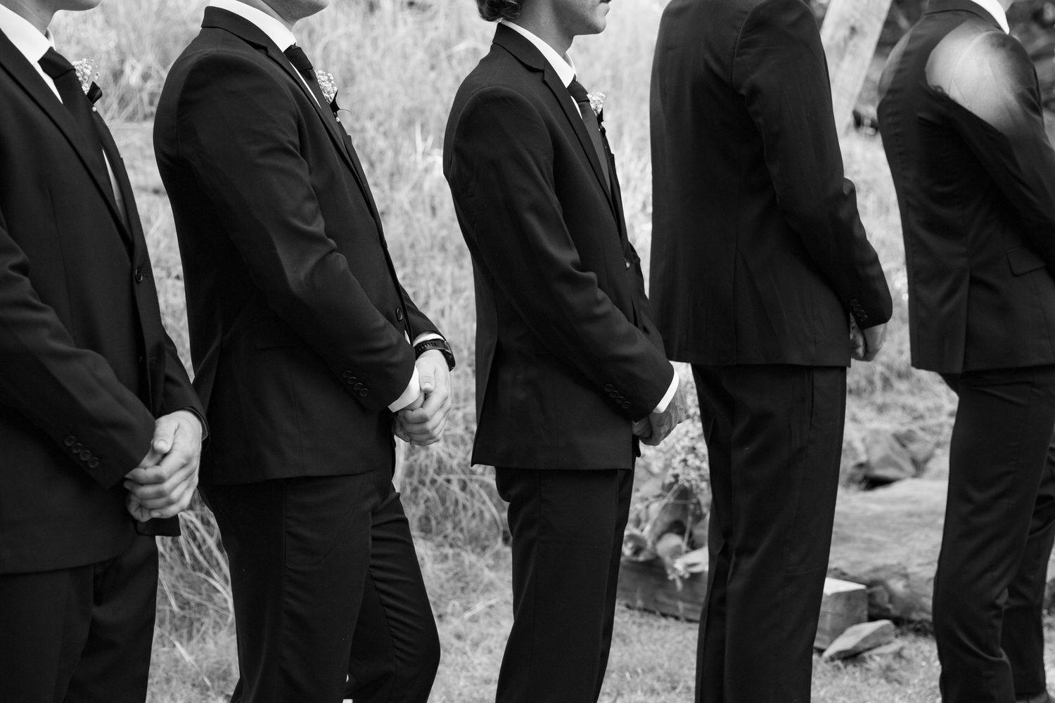 A line of groomsmen in black suits stand in formation at a wedding ceremony.
