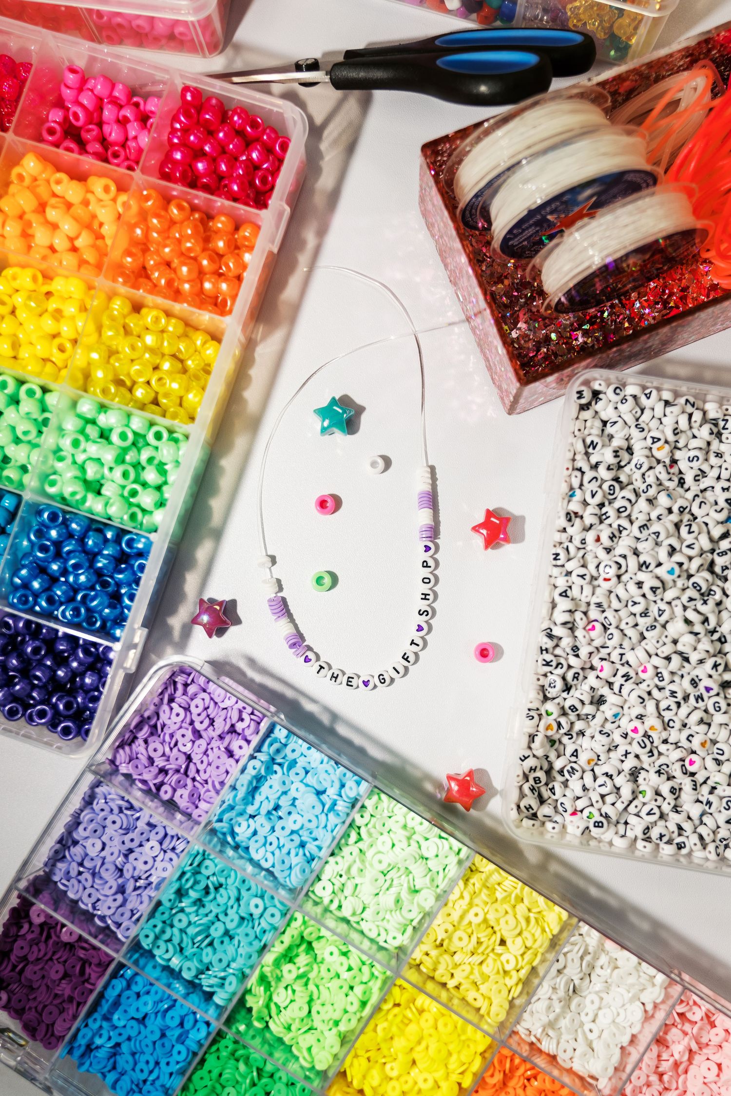 Colorful rainbow assortment of plastic beads organized in clear compartments with pattern templates for craft projects.