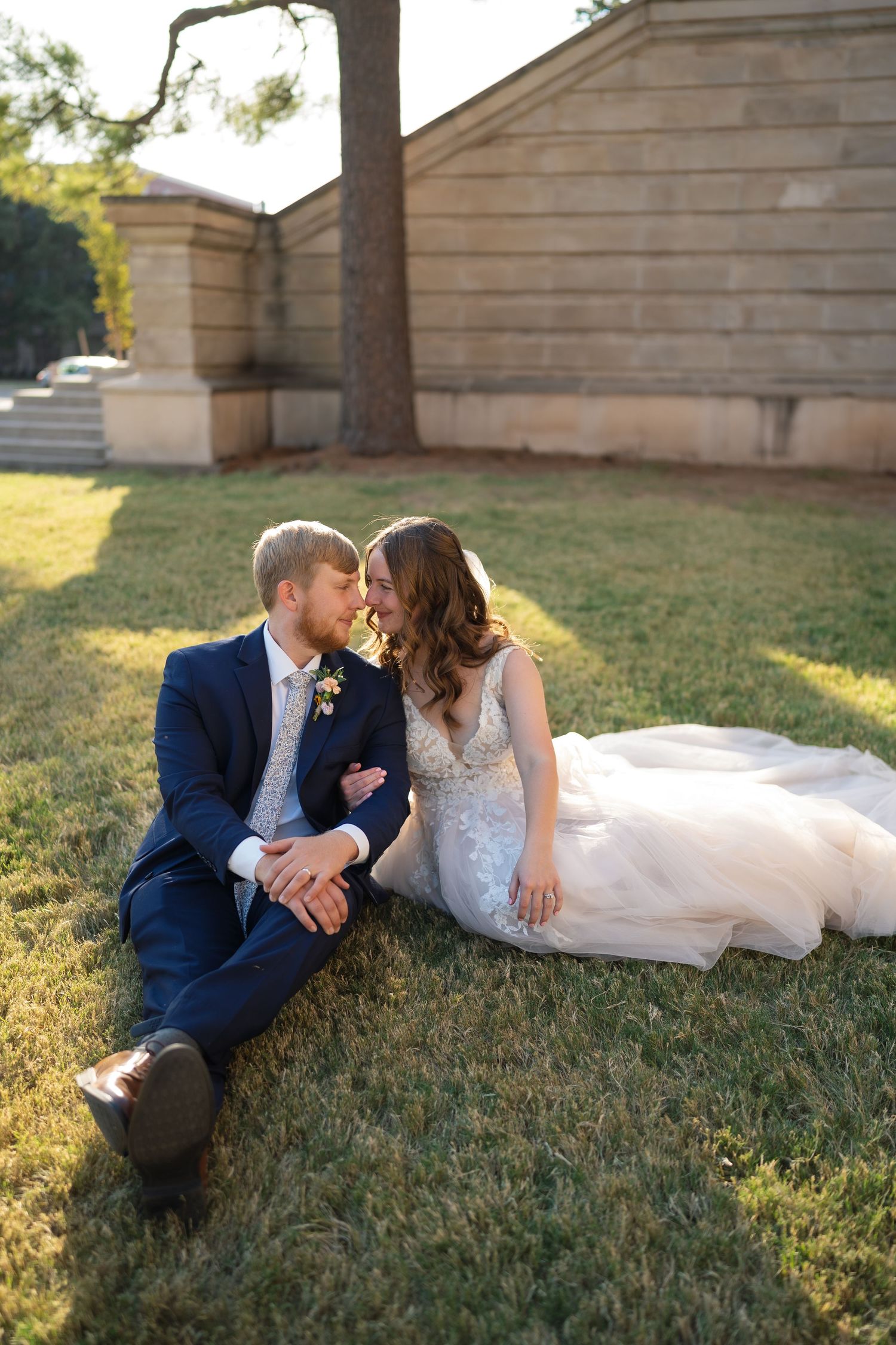 Newlyweds share intimate moments while lounging on grass during sunset portraits.