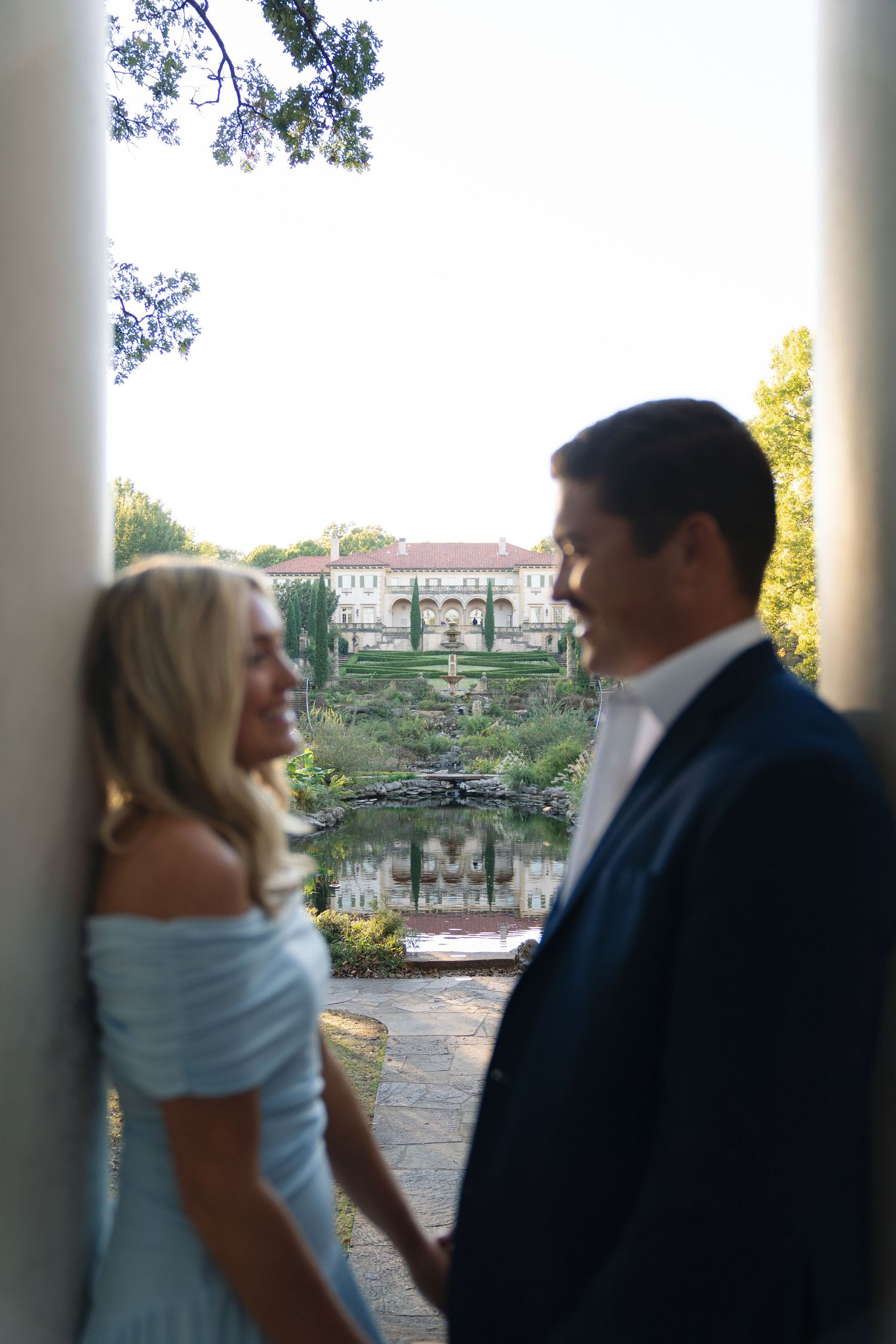 A couple shares an intimate dance moment under white columns with a lake view.