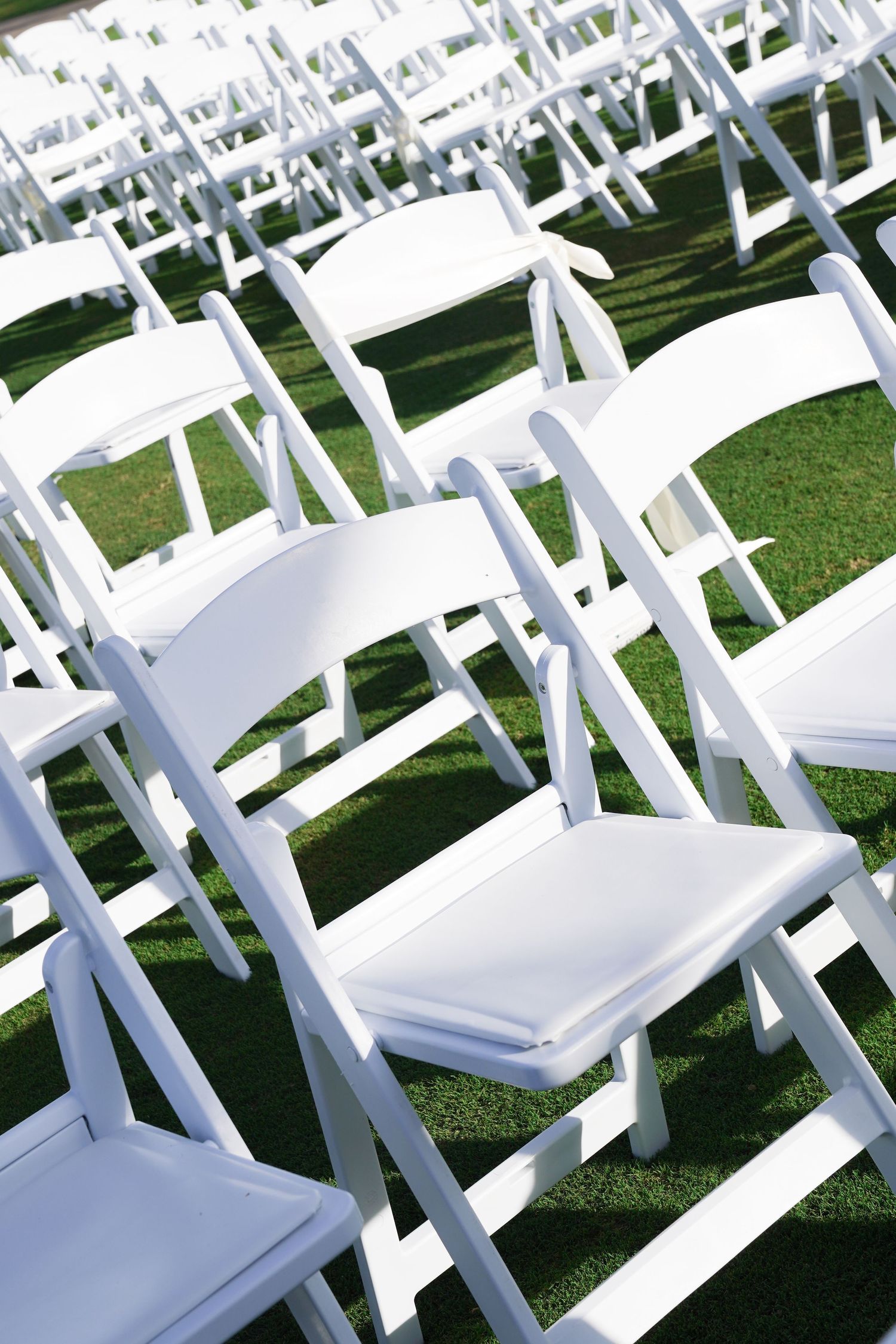 Rows of white folding chairs set up on grass for an outdoor wedding ceremony.