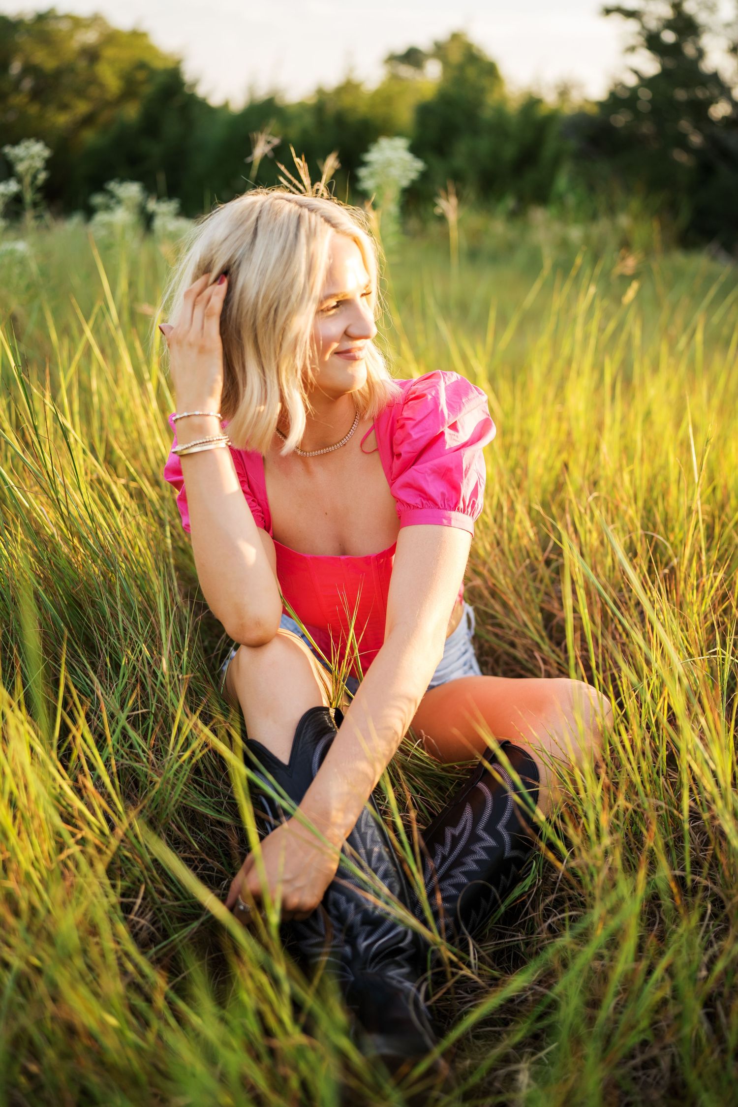 Person in pink top relaxing in tall golden grass during sunset while enjoying peaceful summer evening.