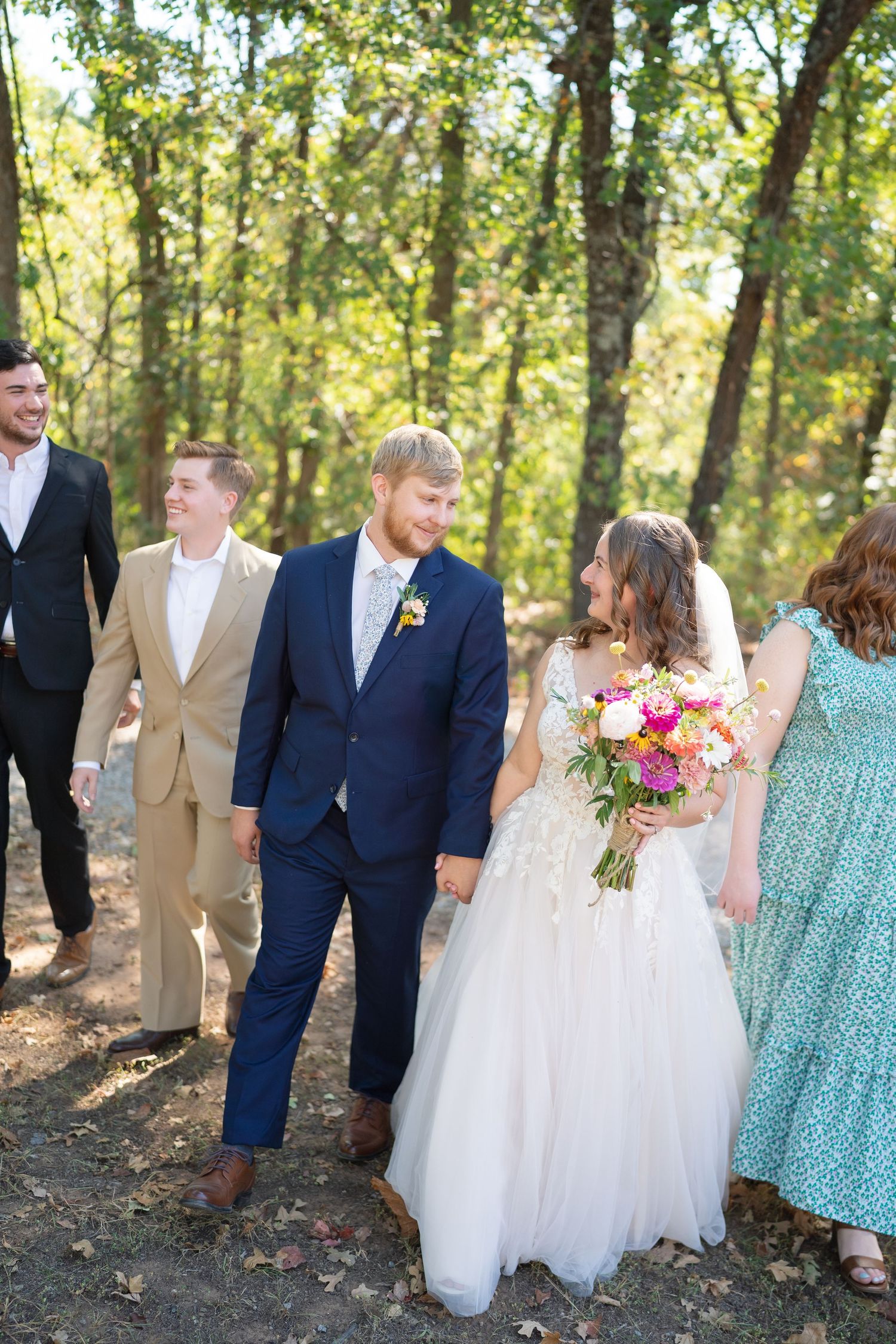 Wedding party walks together through a wooded area wearing navy suits and mint green dresses.