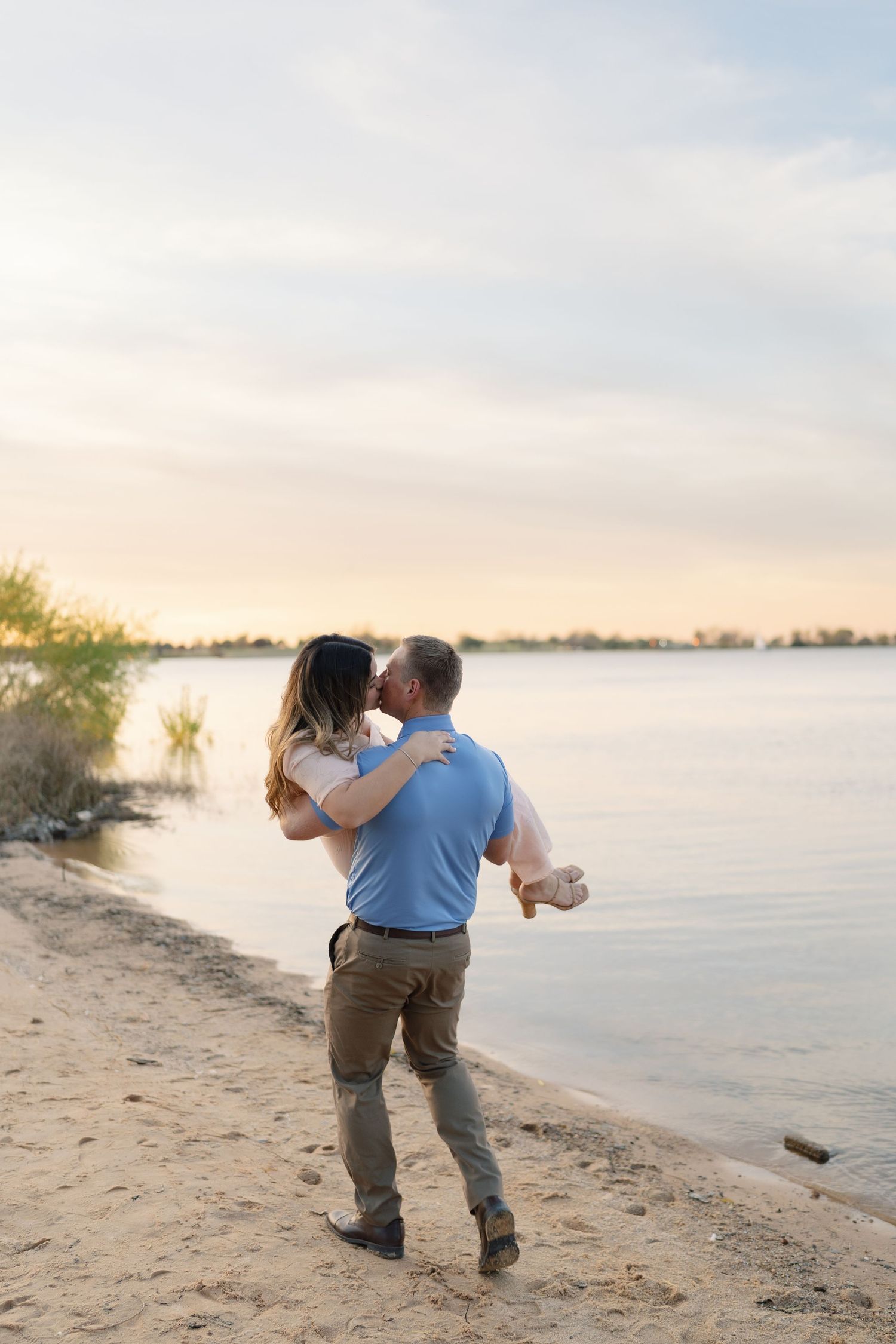 A couple walks away together along a sandy beach shoreline at golden hour.