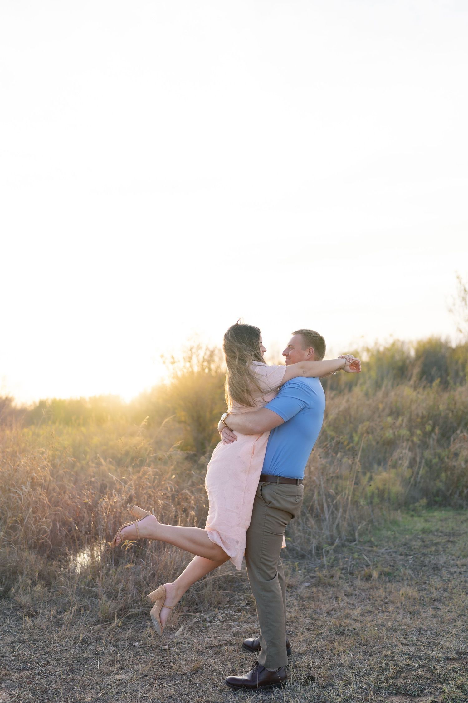 A playful couple spins together in a field during golden hour.