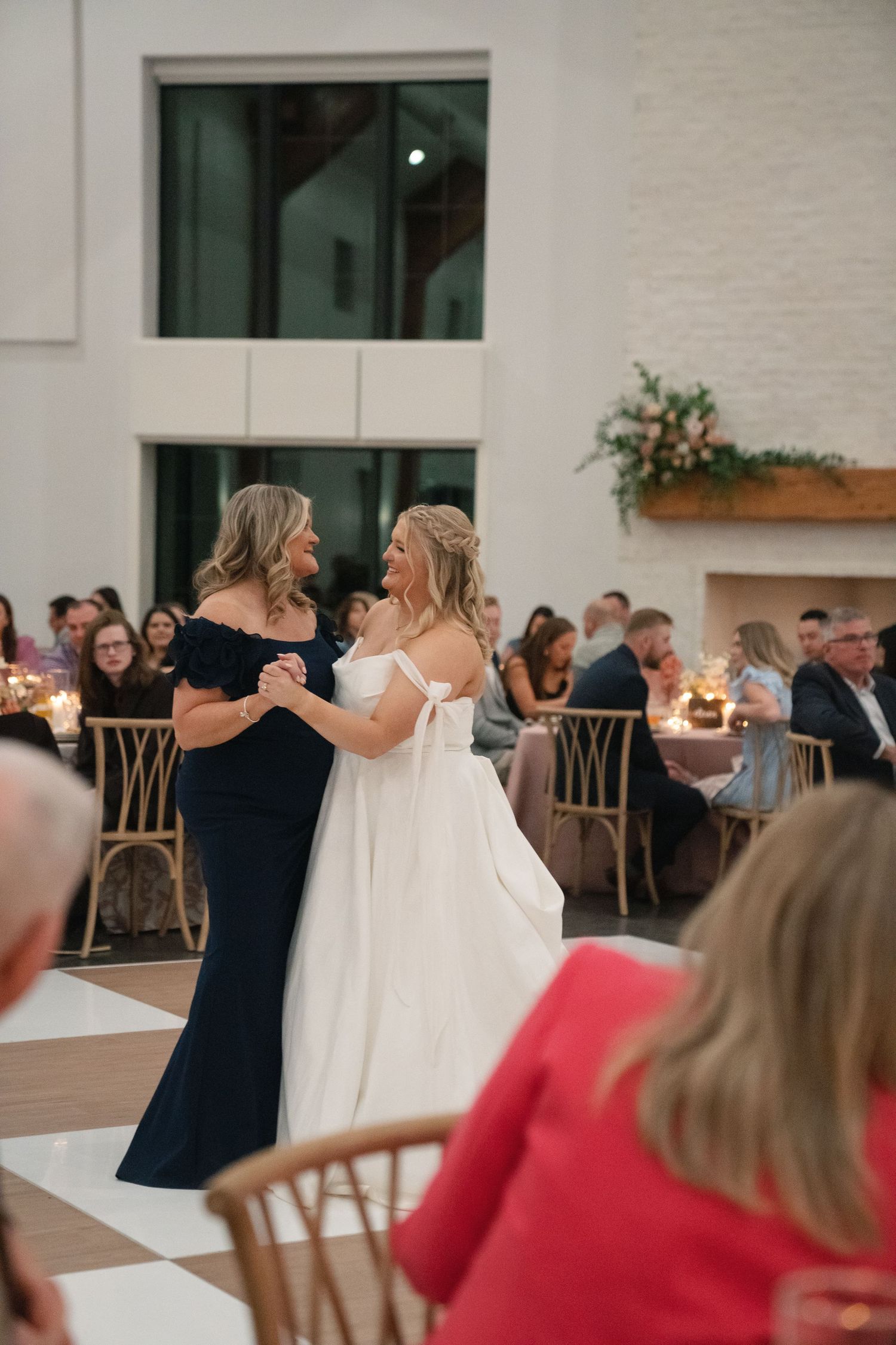 Wedding reception dance in modern white venue with guests watching from tables.