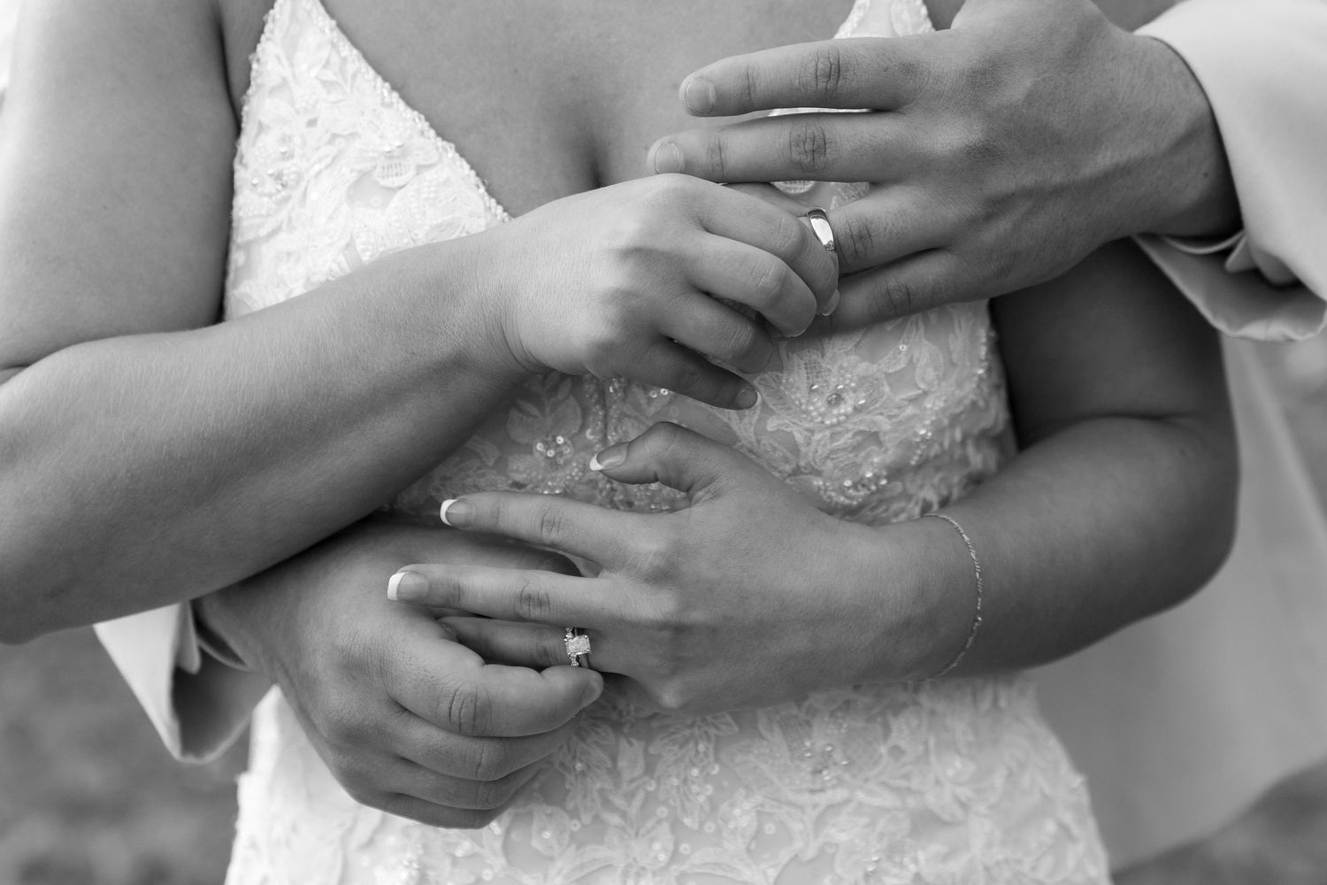 Black and white close-up of hands with wedding rings showing intimate moment.
