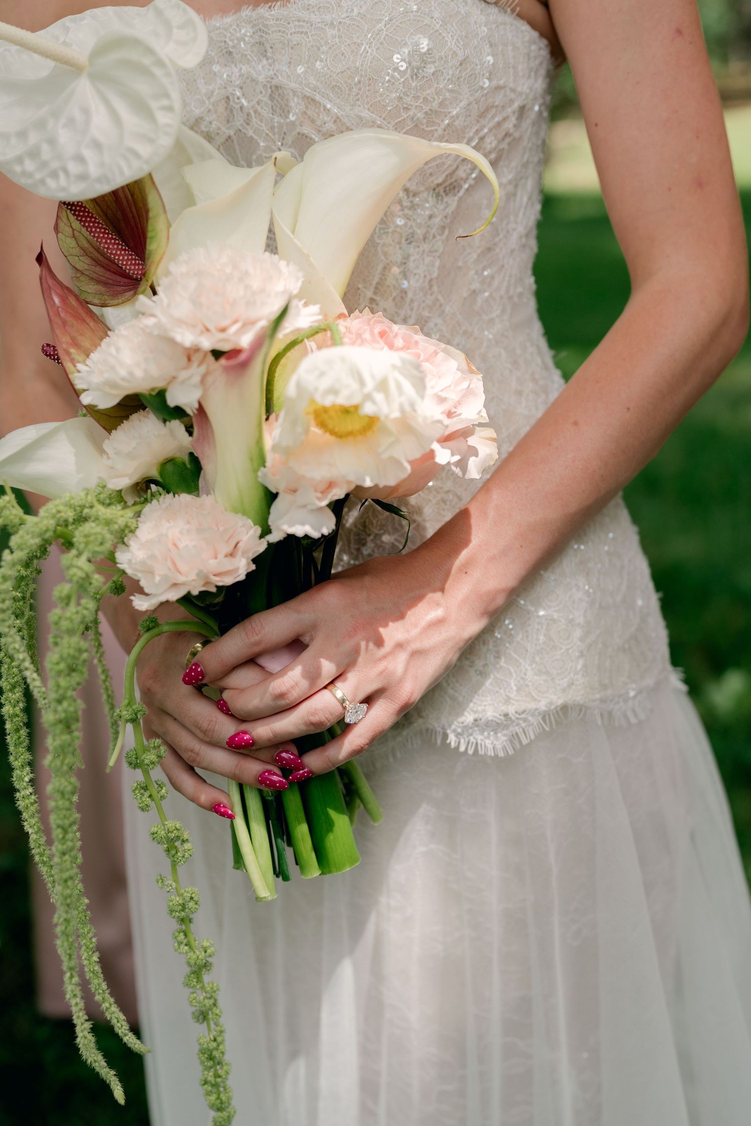 Bride holding elegant wedding bouquet with white calla lilies, pink peonies, and green amaranthus, wearing diamond ring.