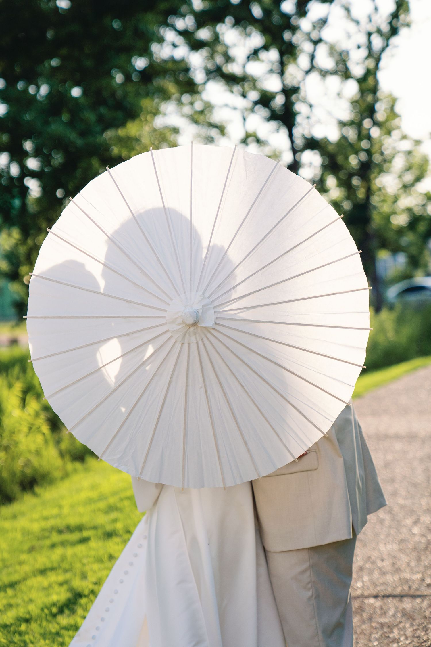White parasol umbrella held against a sunny outdoor backdrop with green trees.