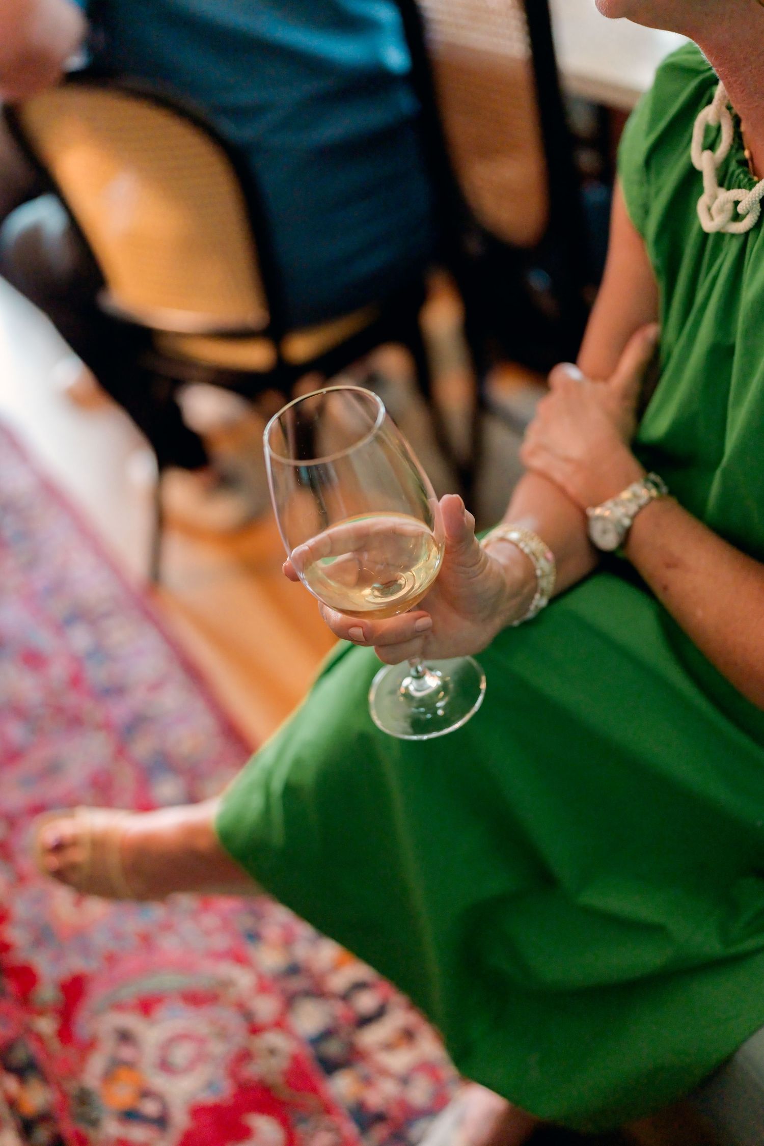 Woman in green dress holds a glass of white wine at an elegant indoor gathering.
