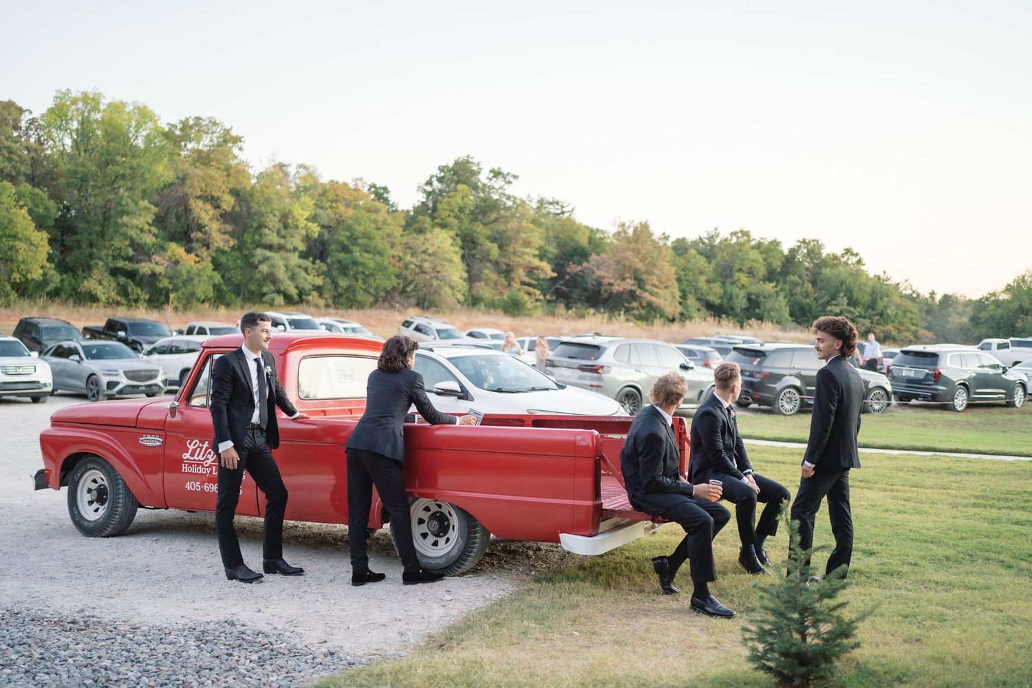 Classic red vintage cars lined up at an outdoor wedding venue with guests mingling nearby.