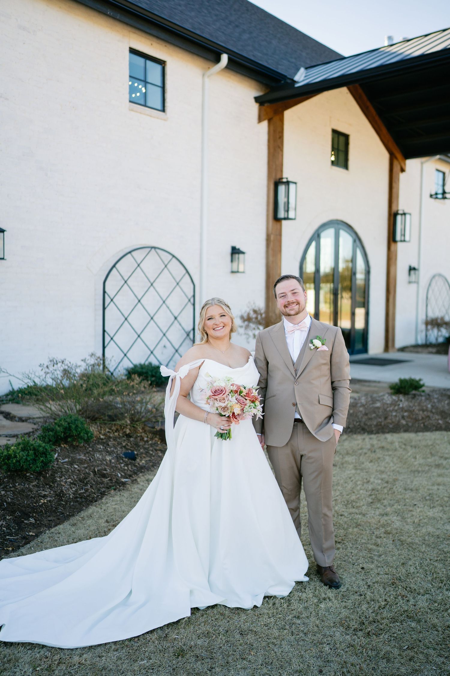 Wedding couple posing for portraits outside a white building with architectural details.
