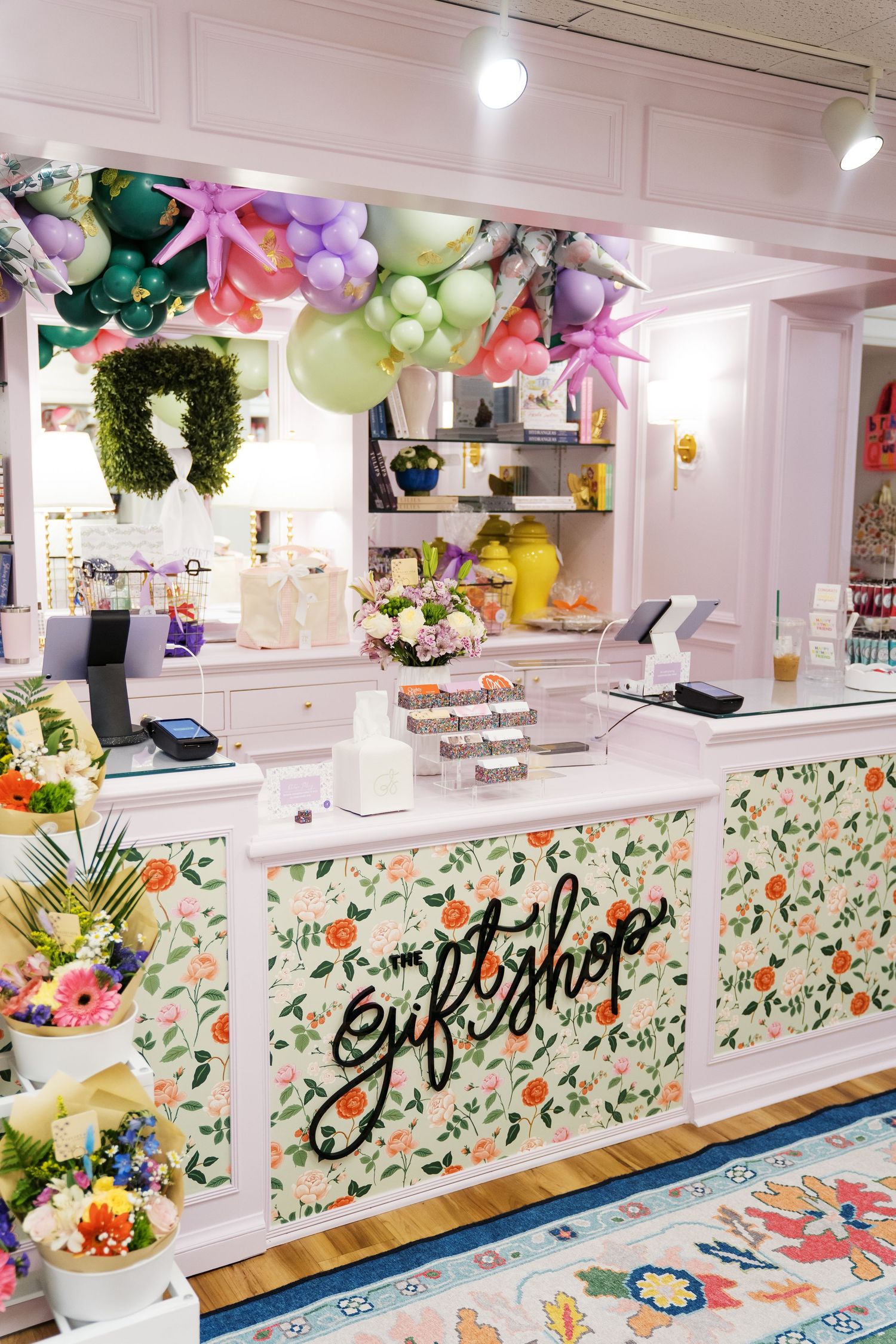 Colorful ice cream shop interior with floral patterns, balloons, and white counters displaying sweet treats and desserts.