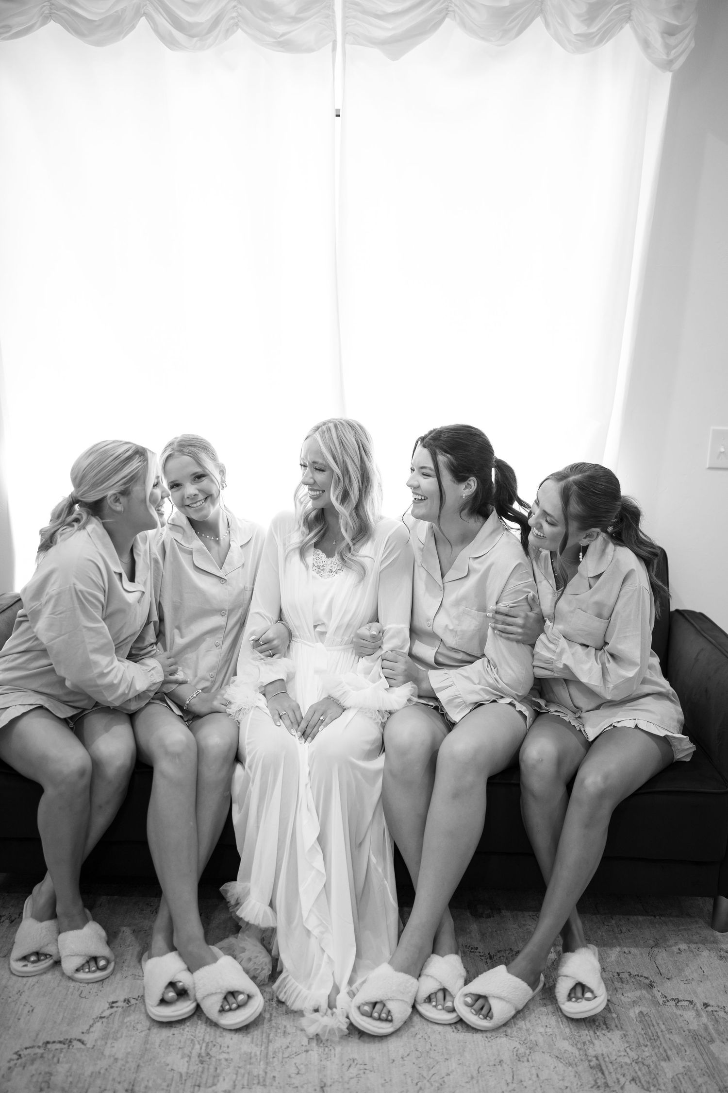 Black and white photo of bridesmaids in matching robes sitting together on a couch.