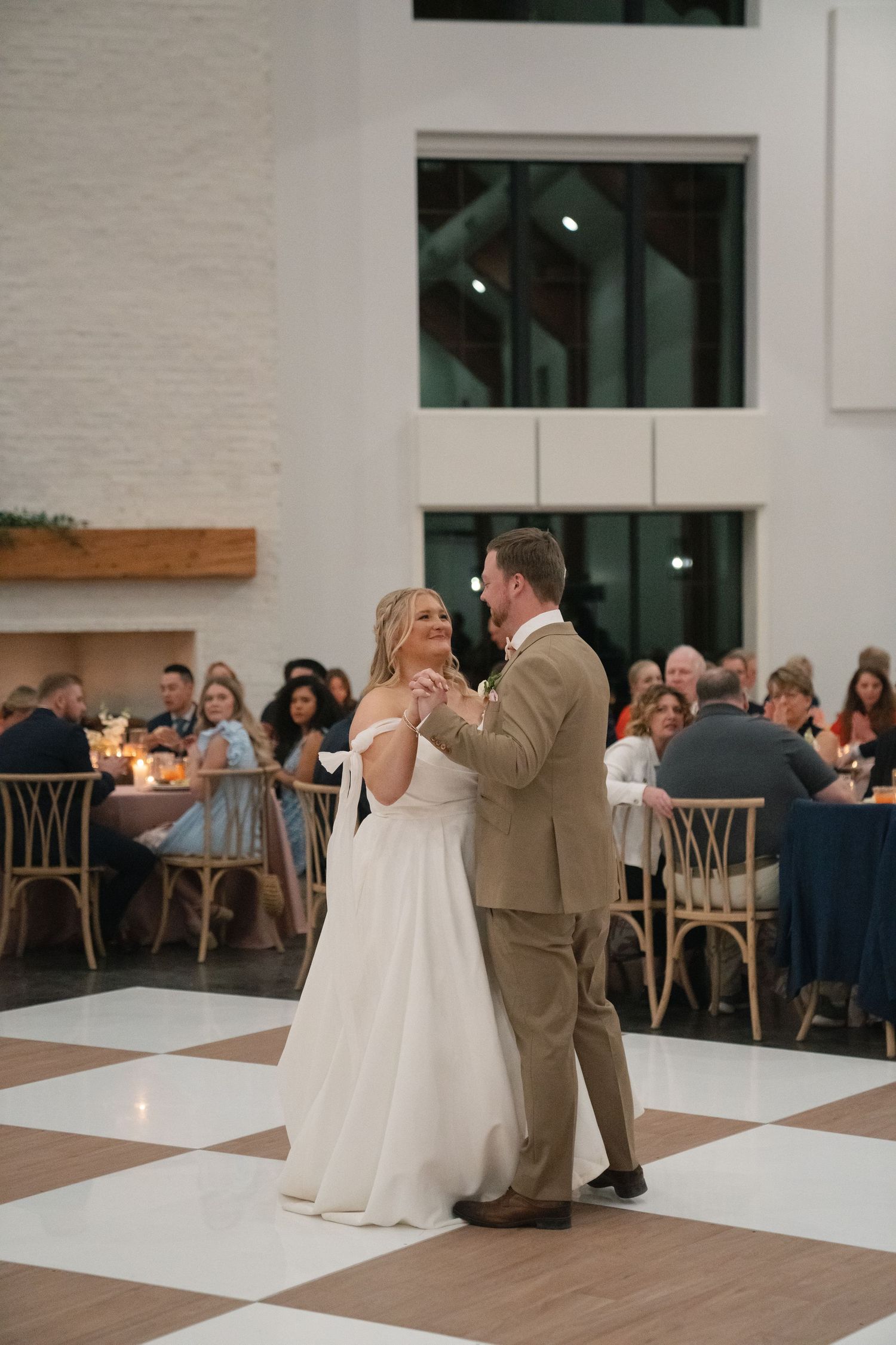 Wedding couple shares first dance in modern reception venue with checkerboard floor.