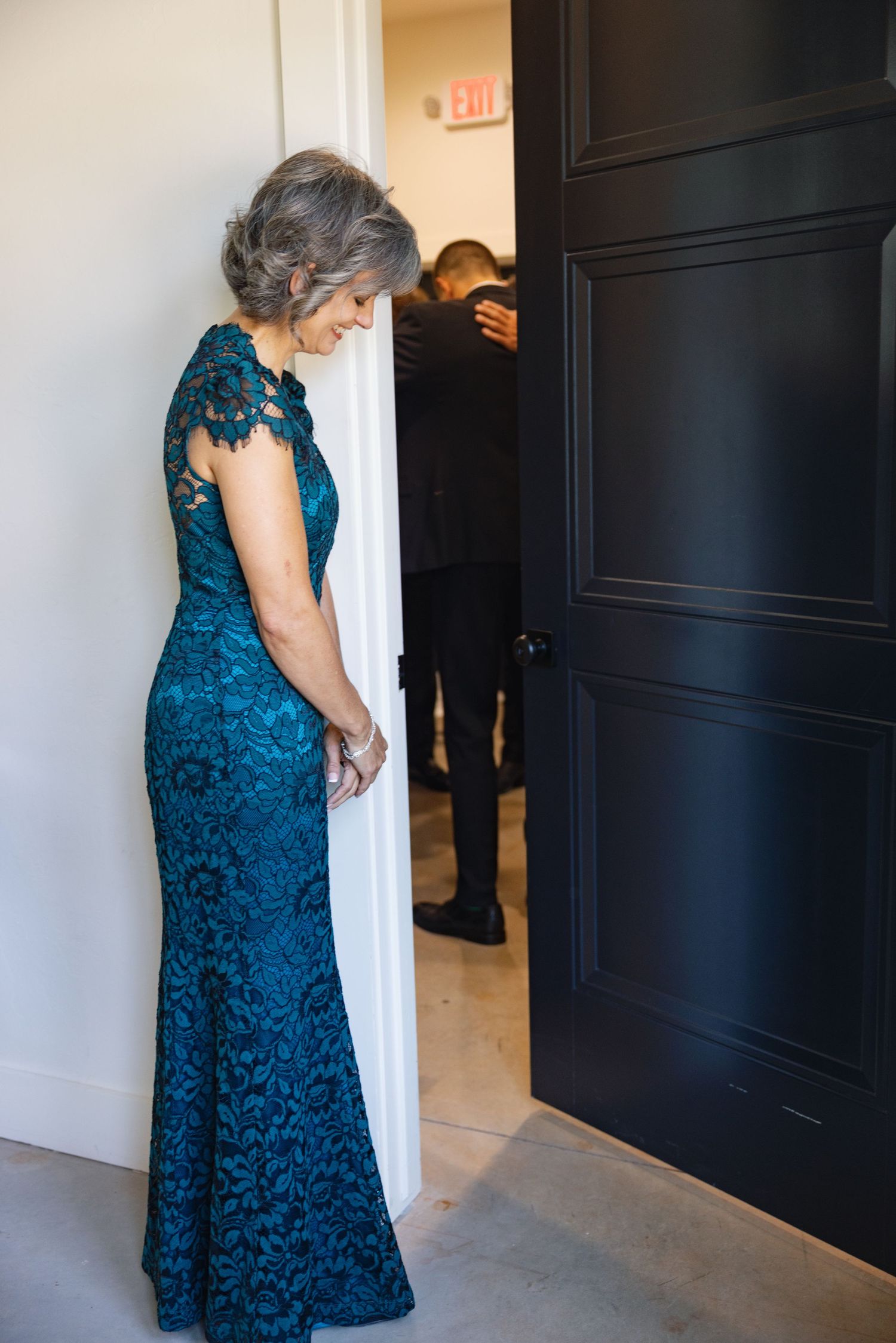 Elegant woman in long blue lace formal dress standing by doorway.