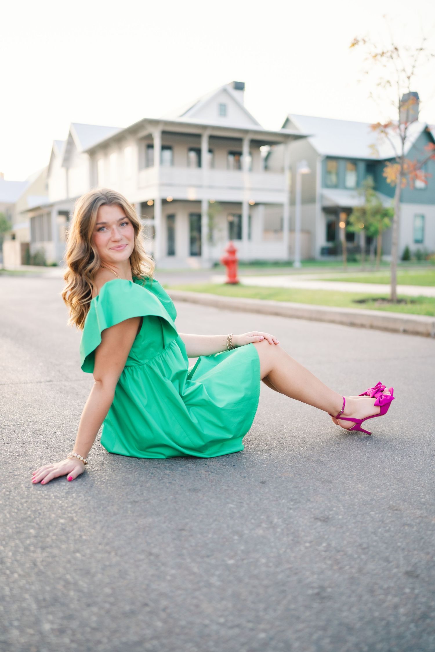 A bright green dress creates contrast against suburban houses in a street photoshoot.