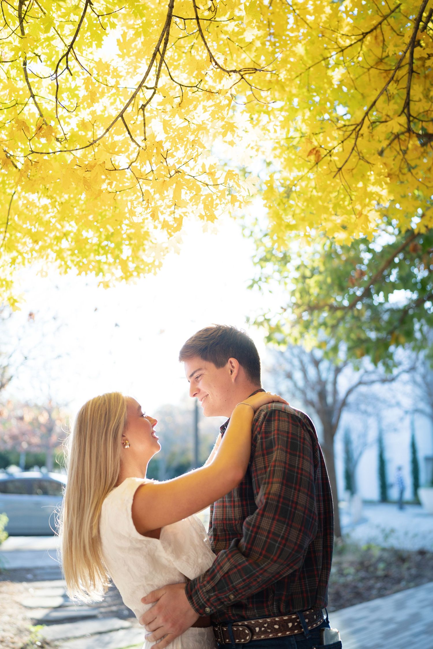 A romantic couple embraces under golden autumn trees in a scenic outdoor setting.